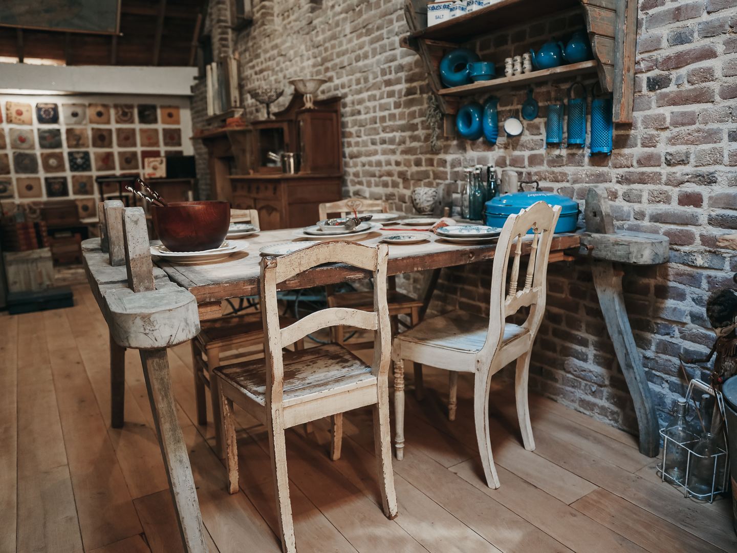 Houten tafel met stoelen en blauw emaille tegen een bakstenen muur bij Brukt & Ateljee