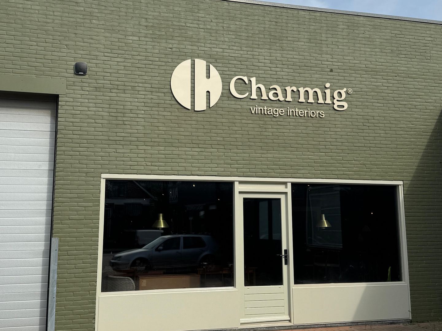 Groen bakstenen pand van Charmig met wit logo boven de glazen ingang en grote etalageramen
