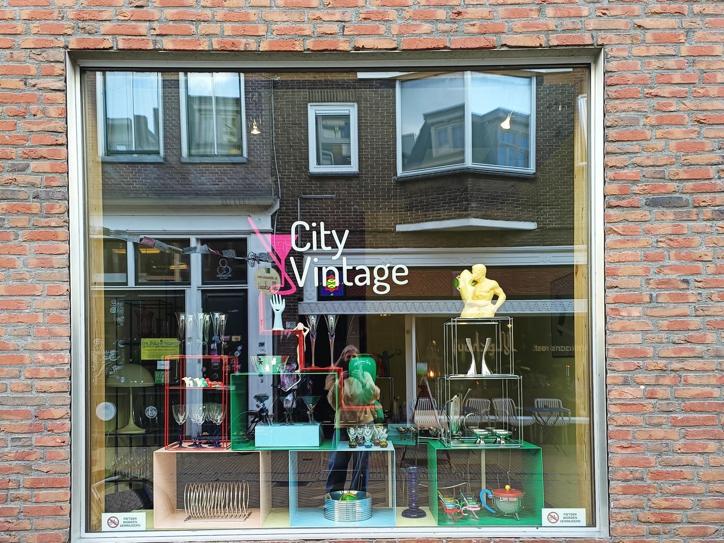 Etalage van City Vintage in een bakstenen gevel met de naam op het raam en kleurrijk glaswerk erachter