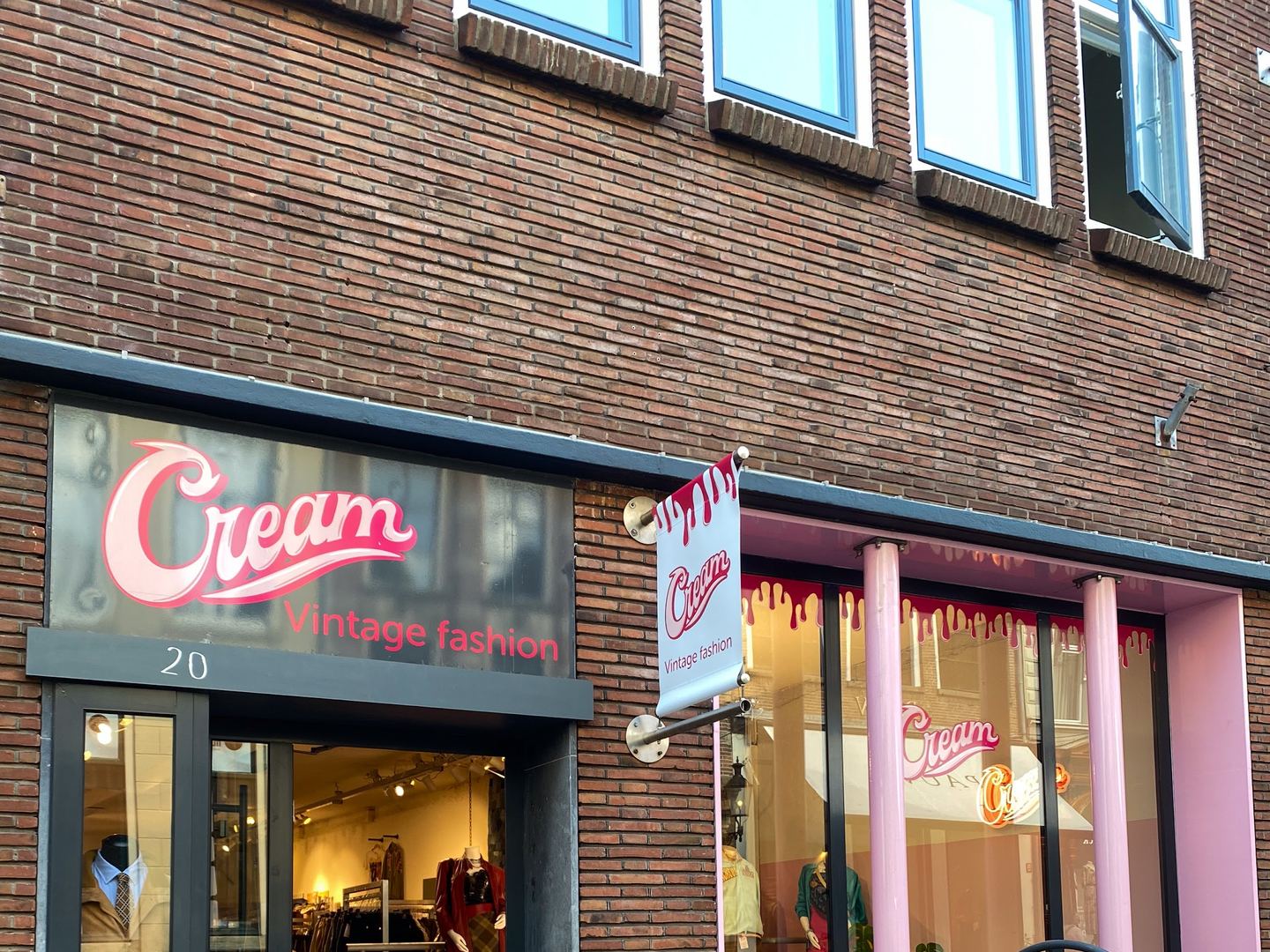 Bakstenen gevel van Cream met roze naambord, open glazen deur, etalage met roze pilaren en een stoepbord
