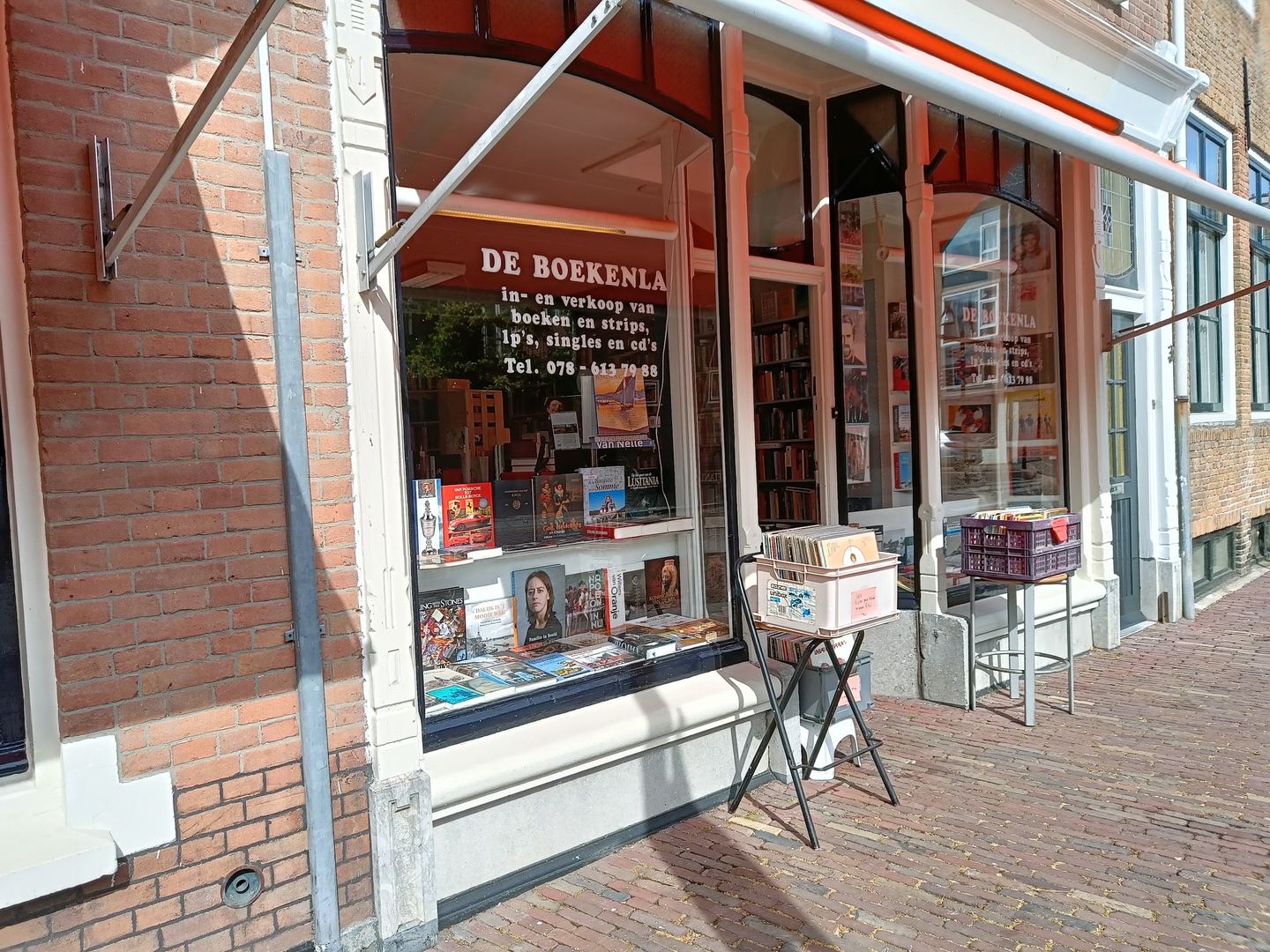 Gevel van De Boekenla met boeken in de etalage en een bak met platen op de stoep