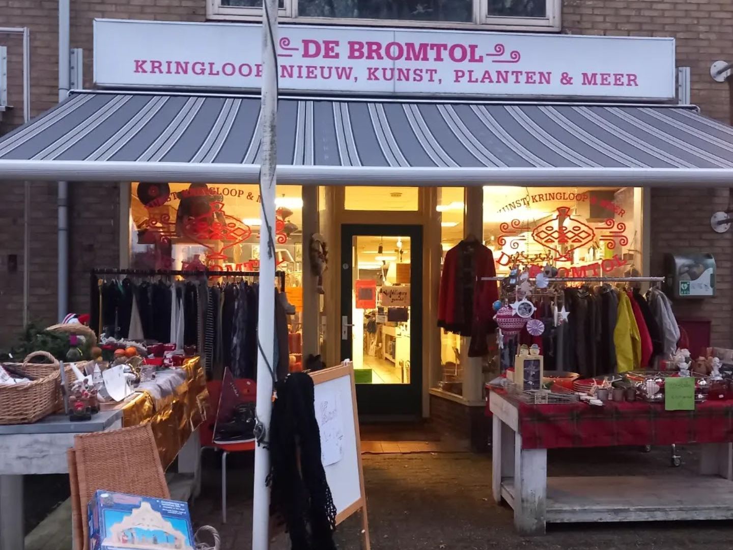 Winkelpui van Kringloopwinkel De Bromtol met luifel en kledingrekken voor de deur