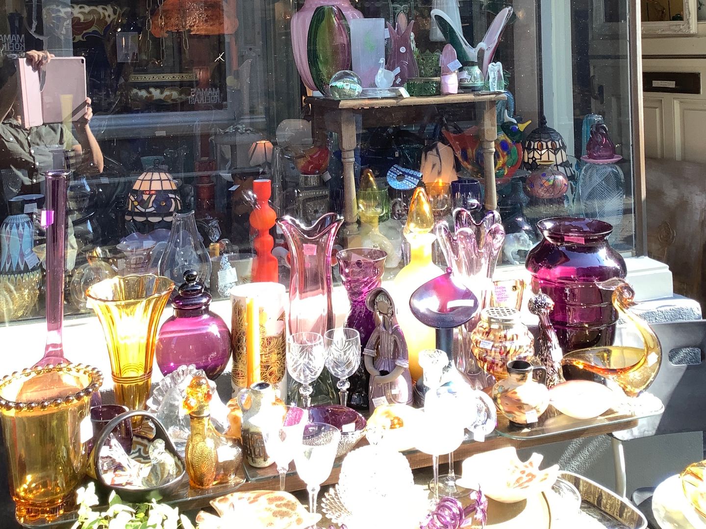 Etalage van De Colibri Antiek en Curiosa met gekleurd glaswerk en een naambord