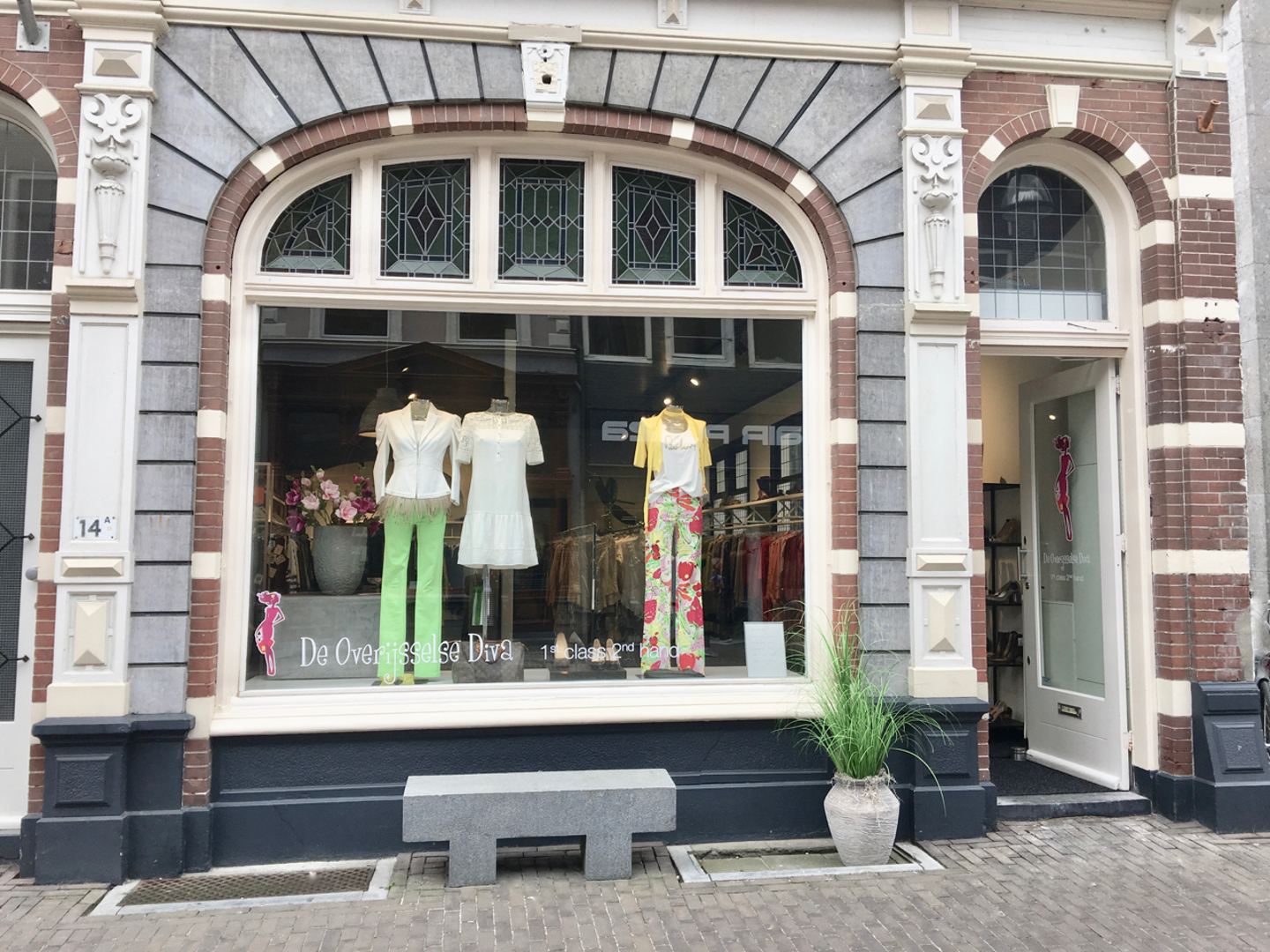 Gevel van De Diva met boogvormige etalage, paspoppen in kleurige designerkleding en een open witte deur