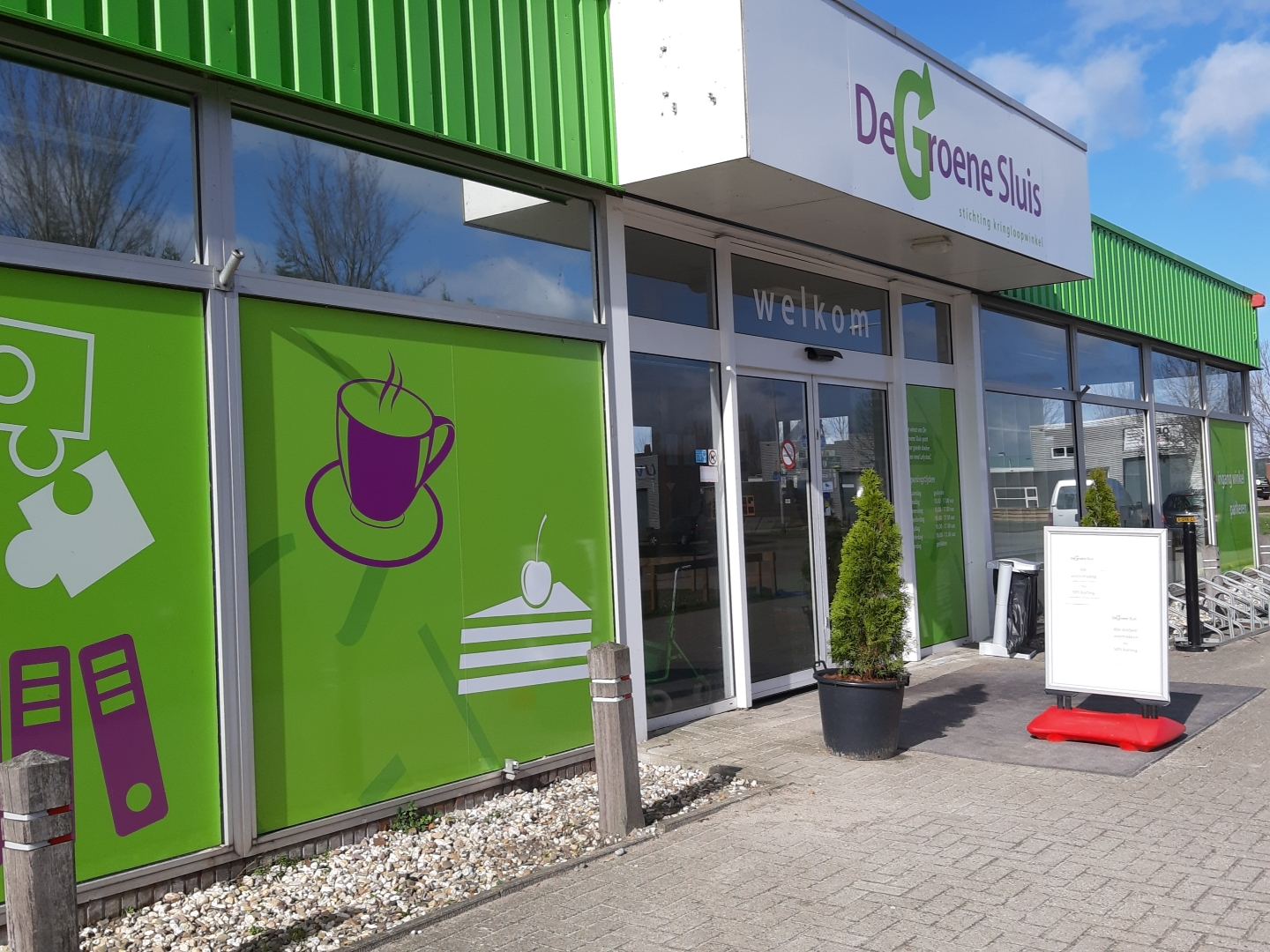 Ingang van kringloopwinkel De Groene Sluis met groene gevel en naambord