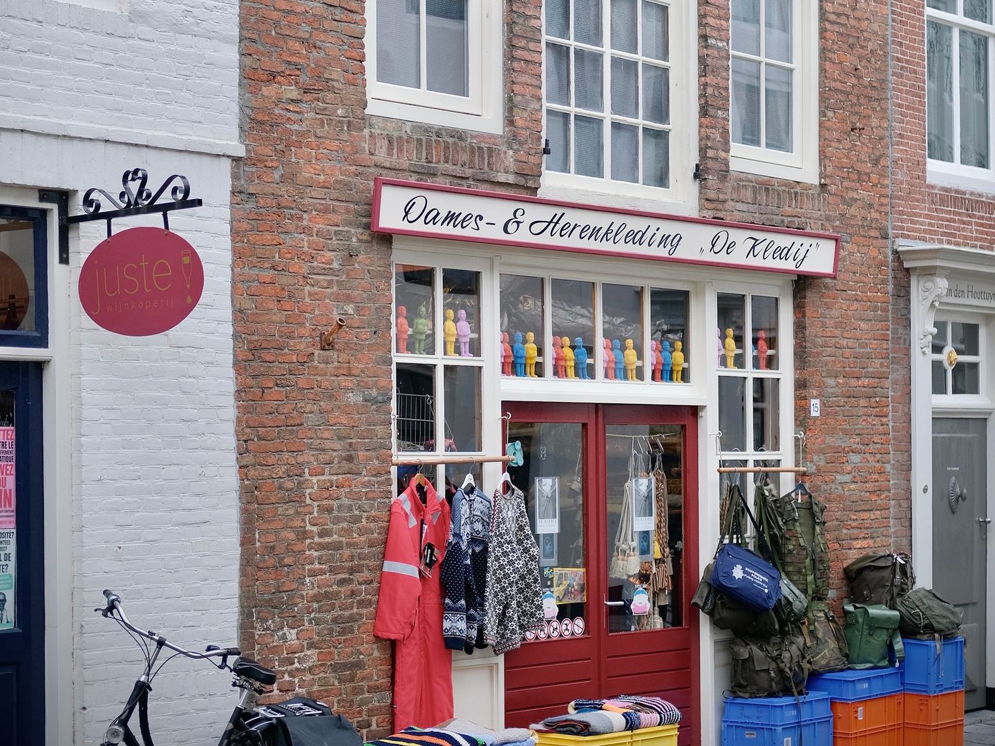 Gevel van De Kledij onder de oude muurreclame Tabaksfabriek, met kleding, tassen en kratten voor de deur
