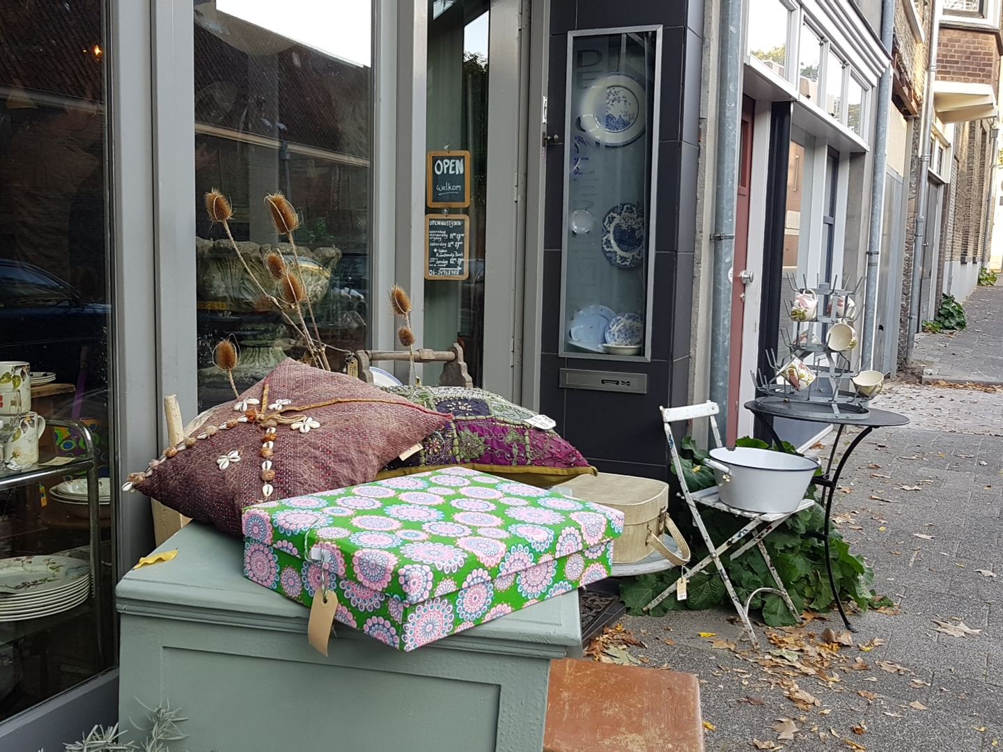 Etalage van De Onderneming met servies en glaswerk, en brocante op de stoep voor de deur