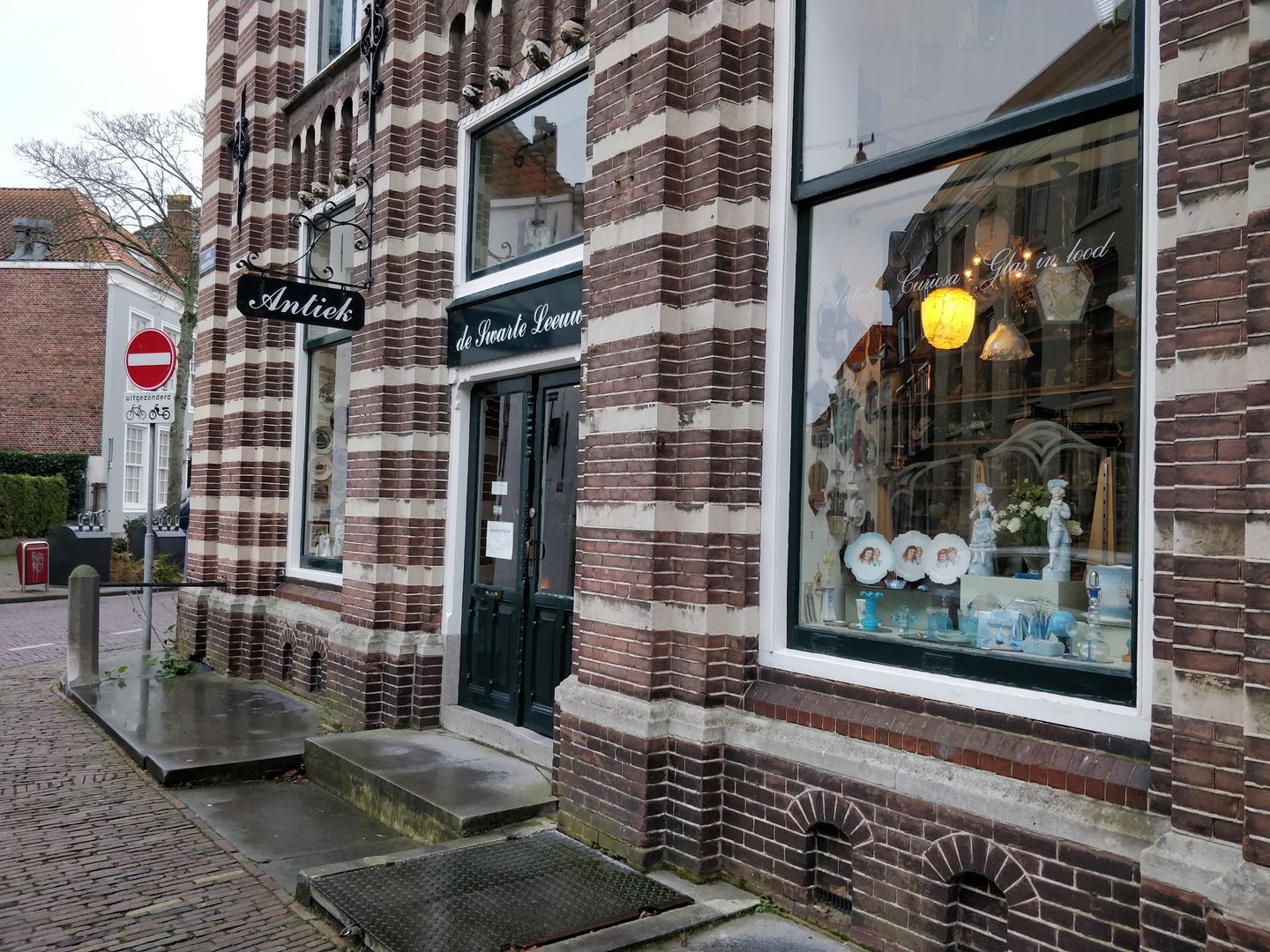 Gestreepte bakstenen gevel van De Swarte Leeuw met uithangbord Antiek en een etalage vol curiosa