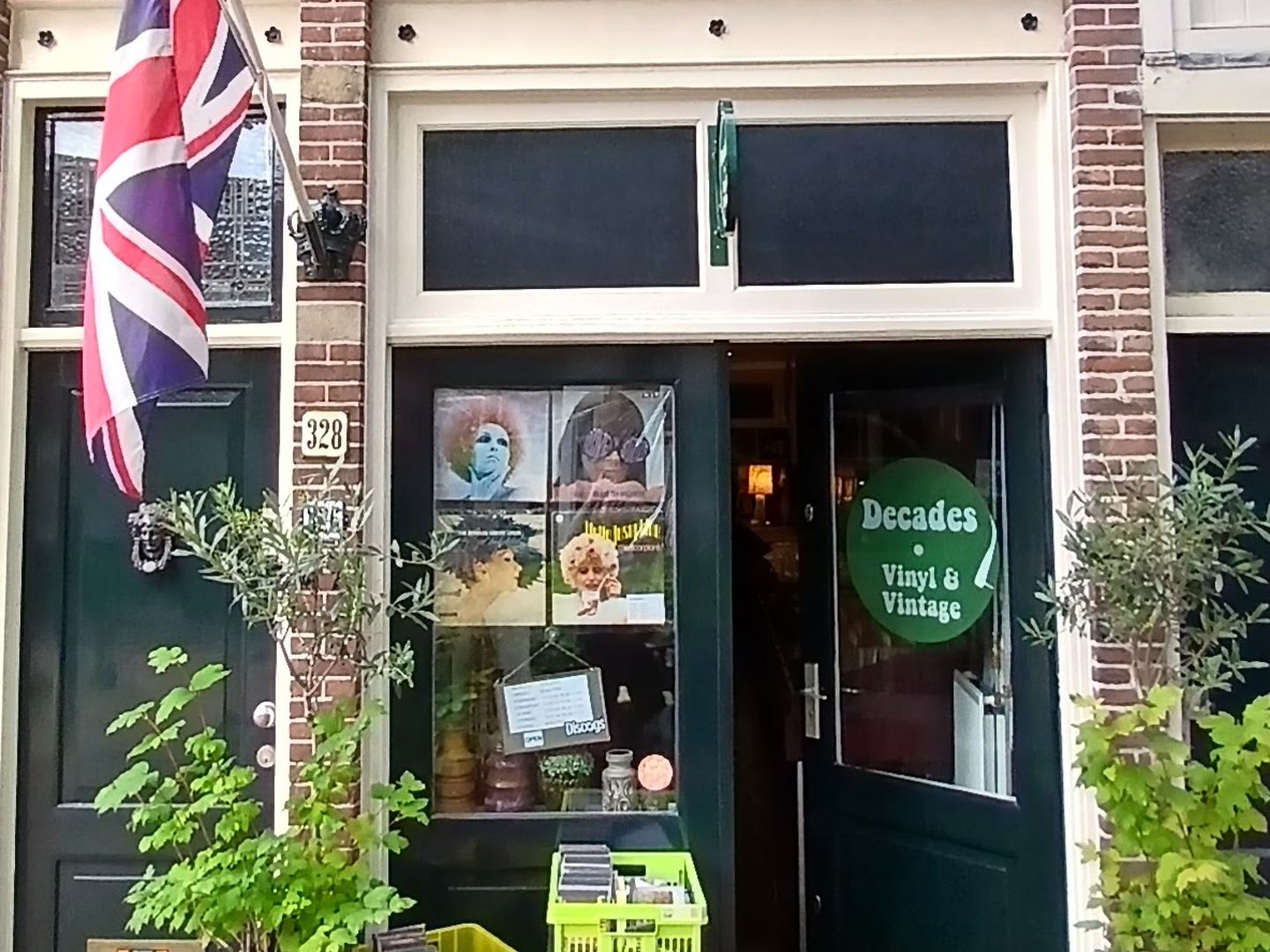 Bakstenen gevel van Decades Vinyl & Vintage met groen deurlogo, platenhoezen in het raam en een Britse vlag