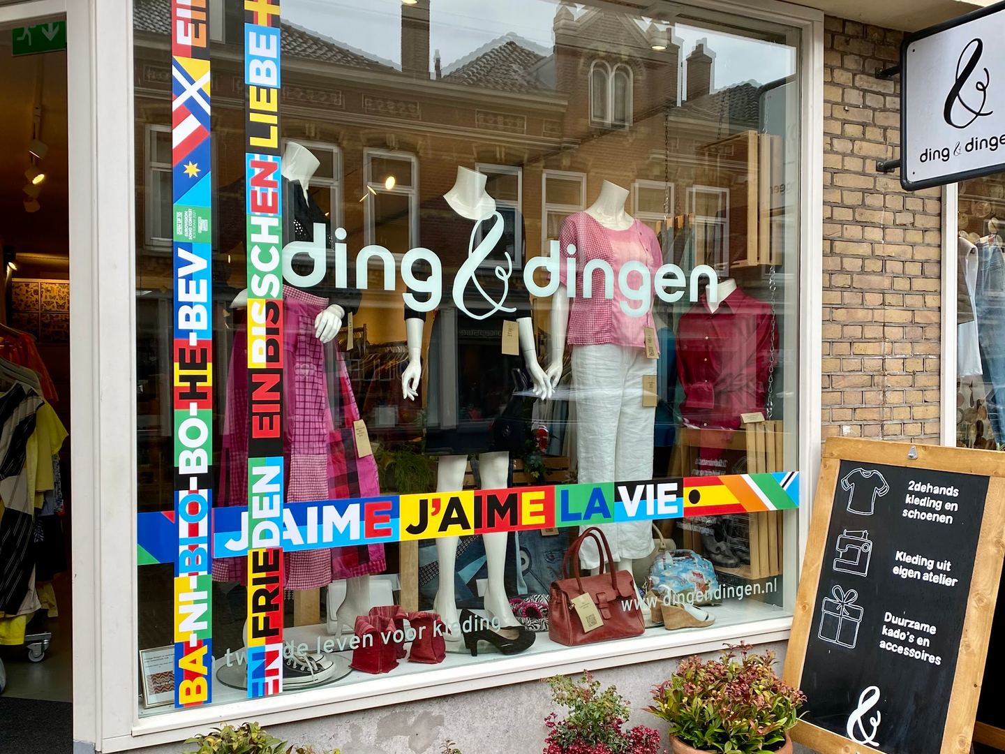 Etalage van Ding & Dingen met kleding op paspoppen, tassen en planten voor de deur