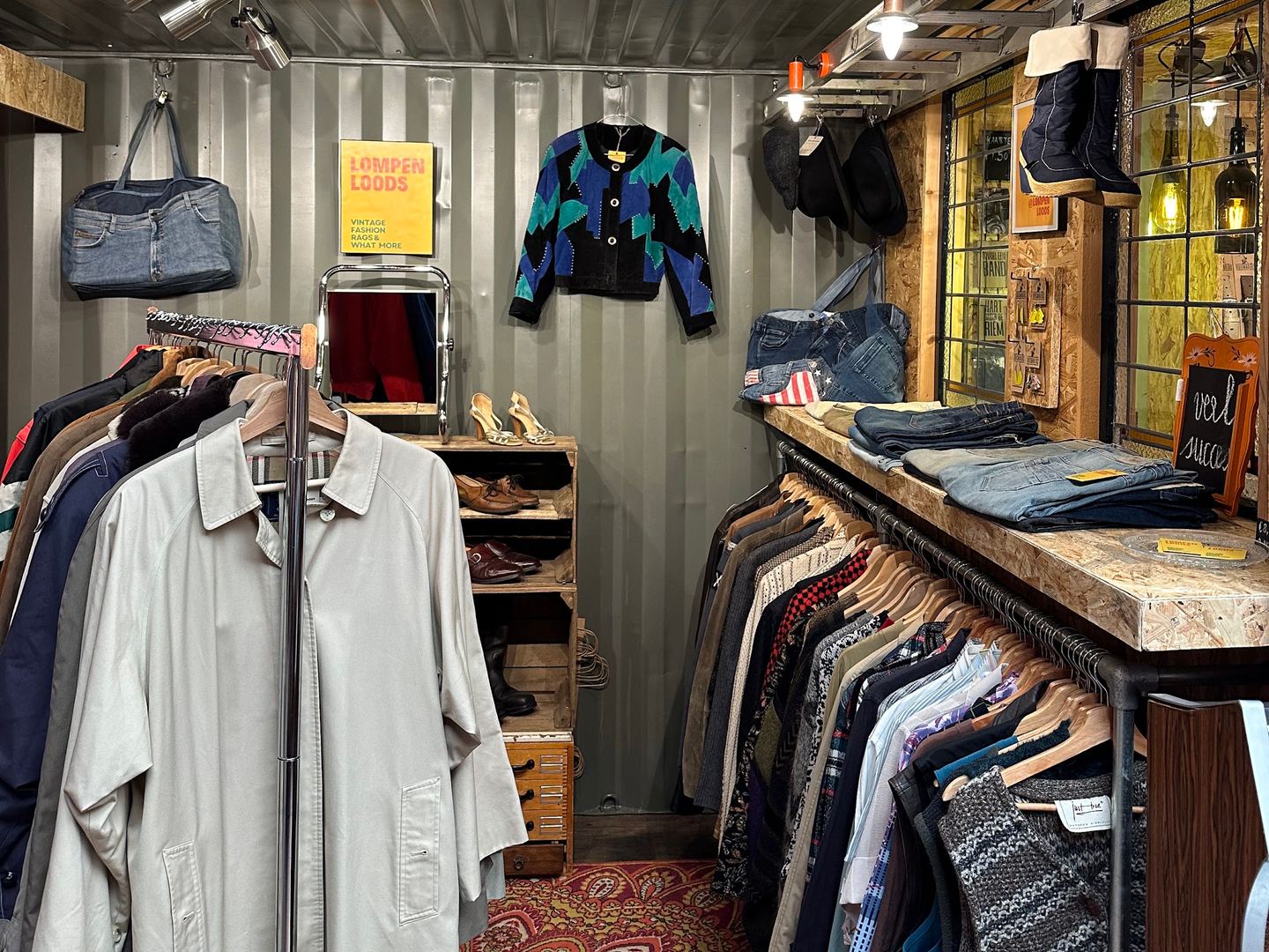Interieur van Doe Lomp vintage met gele LOMP-letters, rekken vol vintage jassen en kleding op een Perzisch tapijt