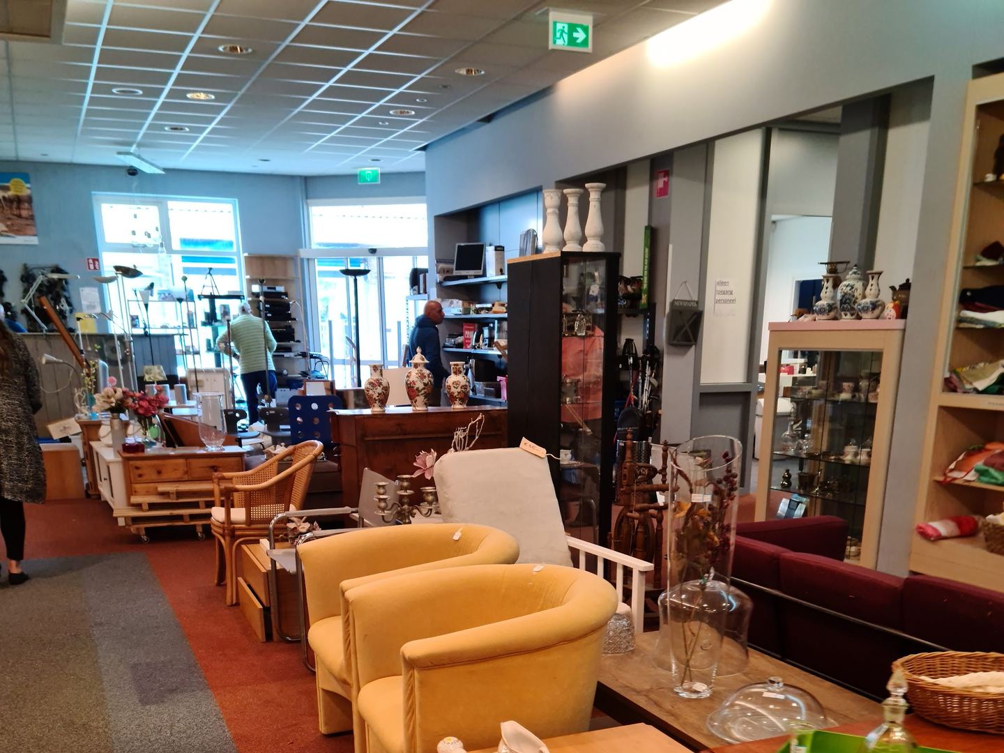 Gele fauteuils, houten tafels en vitrinekasten met servies in Dorcas Winkel Sneek