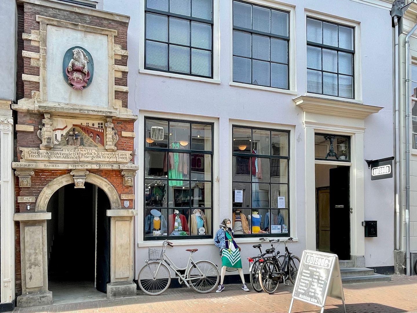 Gevel van Episode met historische stenen poort en etalages vol kleding