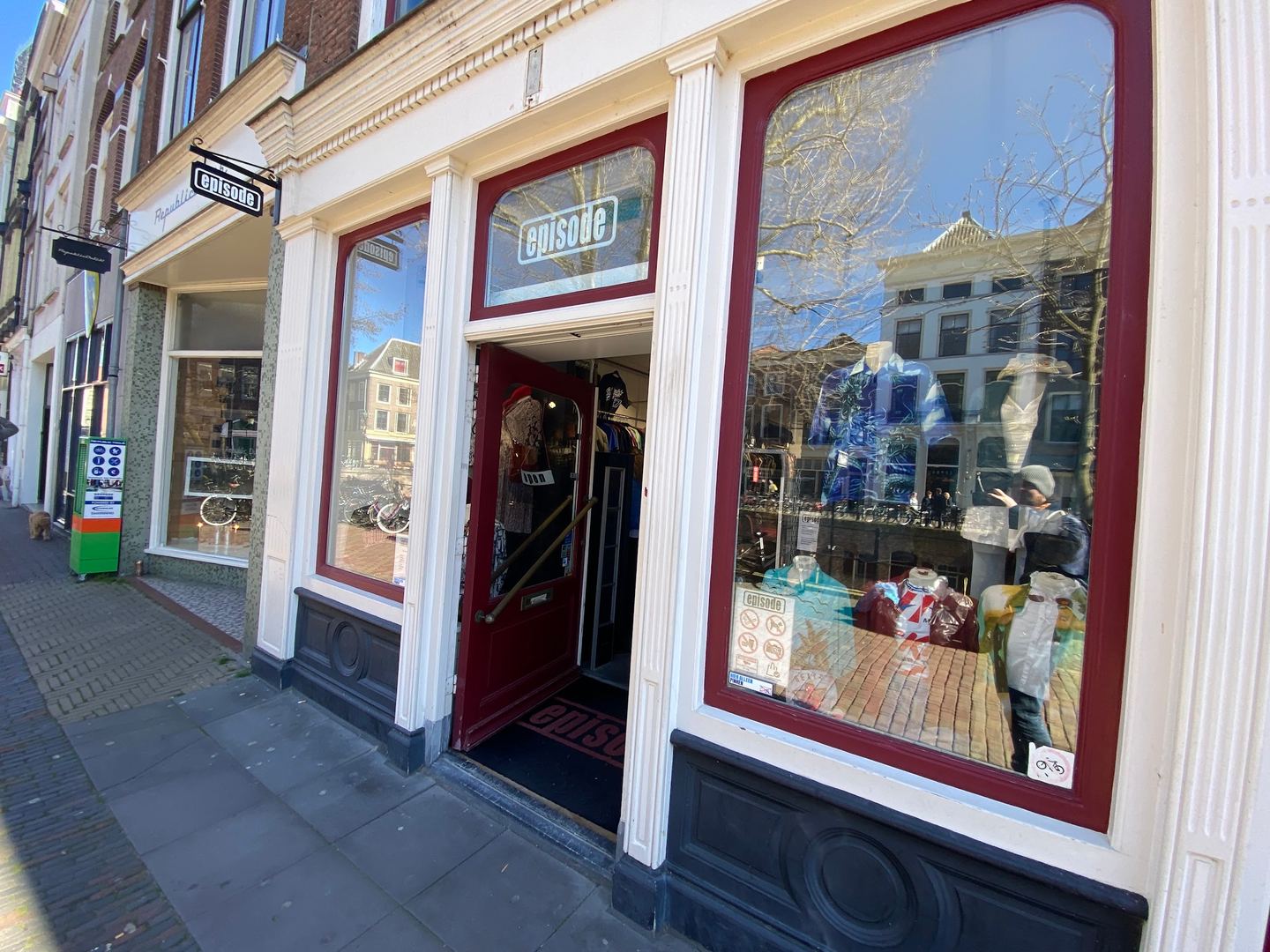 Witte winkelpui van Episode met donkerrode kozijnen, etalages met vintage kleding en een open deur