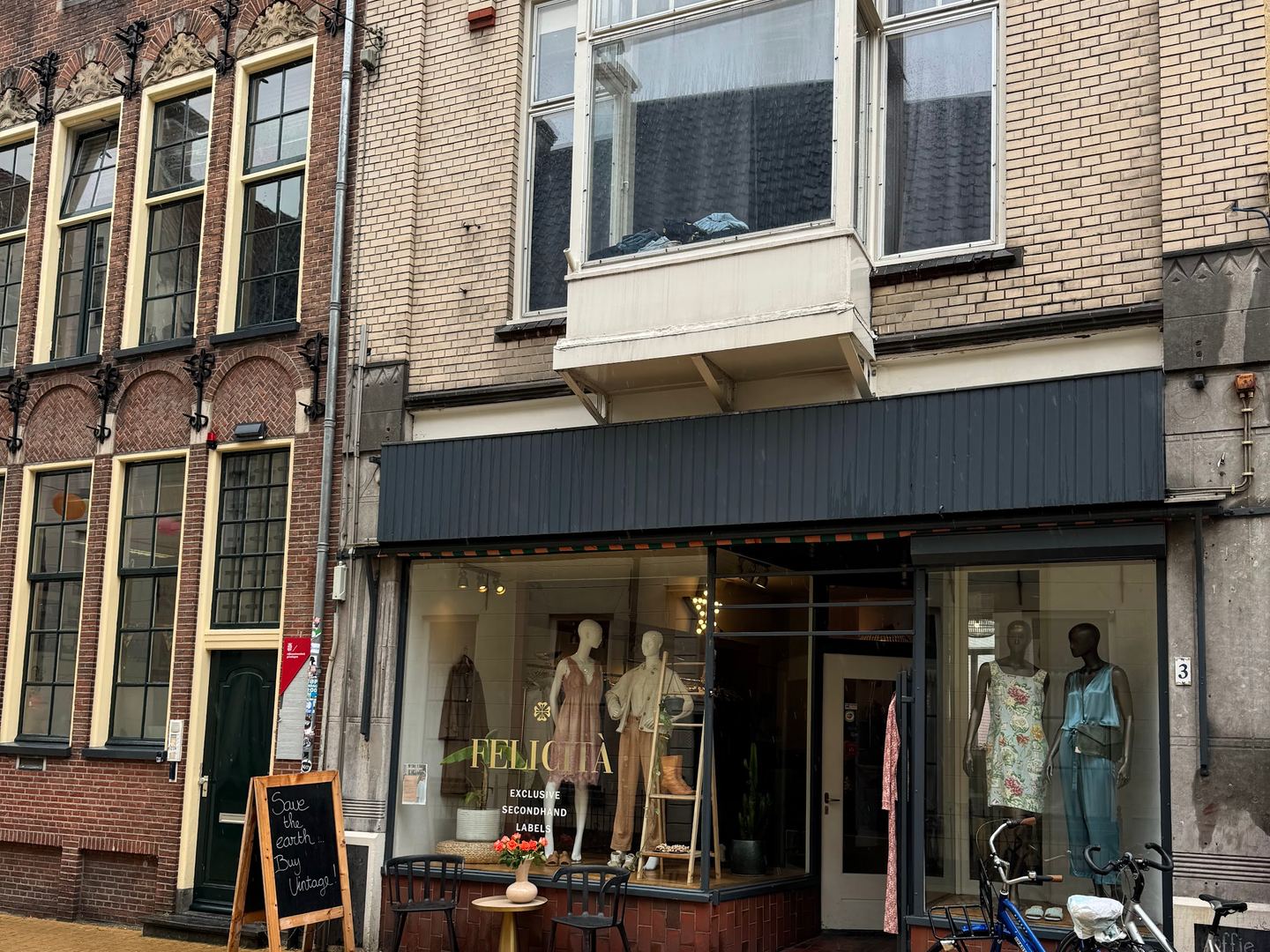 Gevel van Felicità in een oud bakstenen pand met paspoppen in de etalage en een stoepbord voor de deur