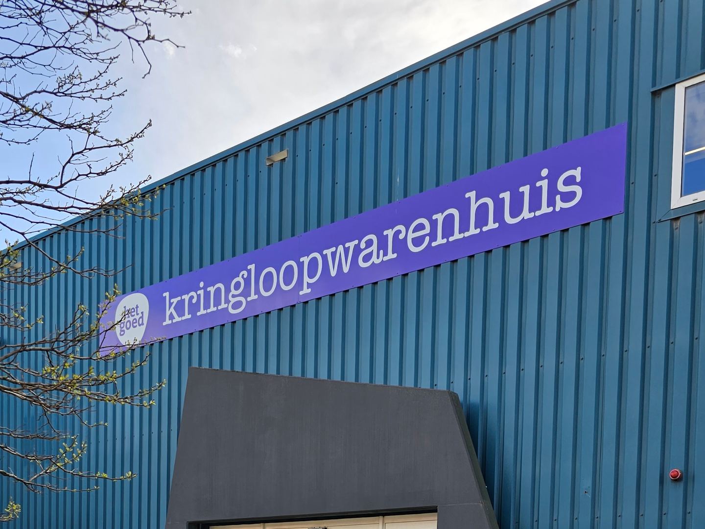 Gevel van Kringloopwarenhuis Het Goed Vlaardingen met het paarse naambord boven de glazen ingang