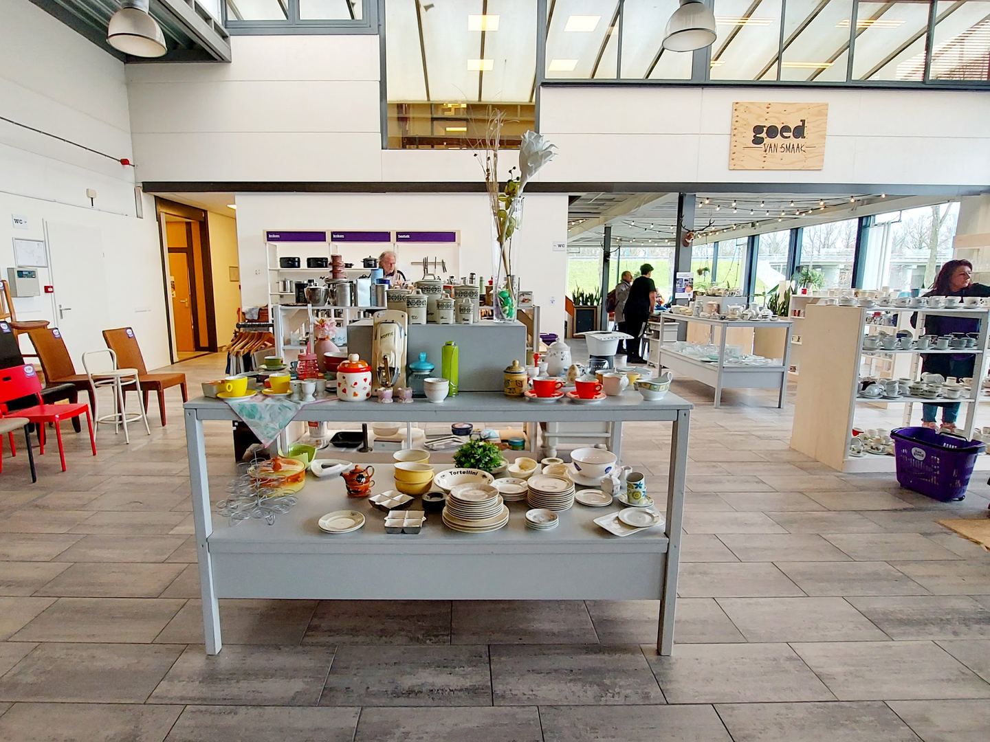 Tafel met servies en kleurrijke kopjes in Het Goed Zoetermeer, met het lunchcafé op de achtergrond