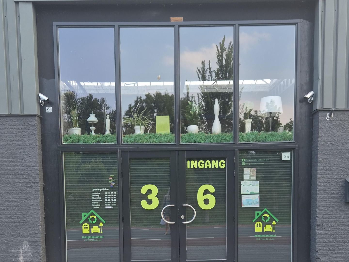 Ingang van Kringloopwinkel Het Tweede Leven met glazen deuren, logo en openingstijden op de ramen