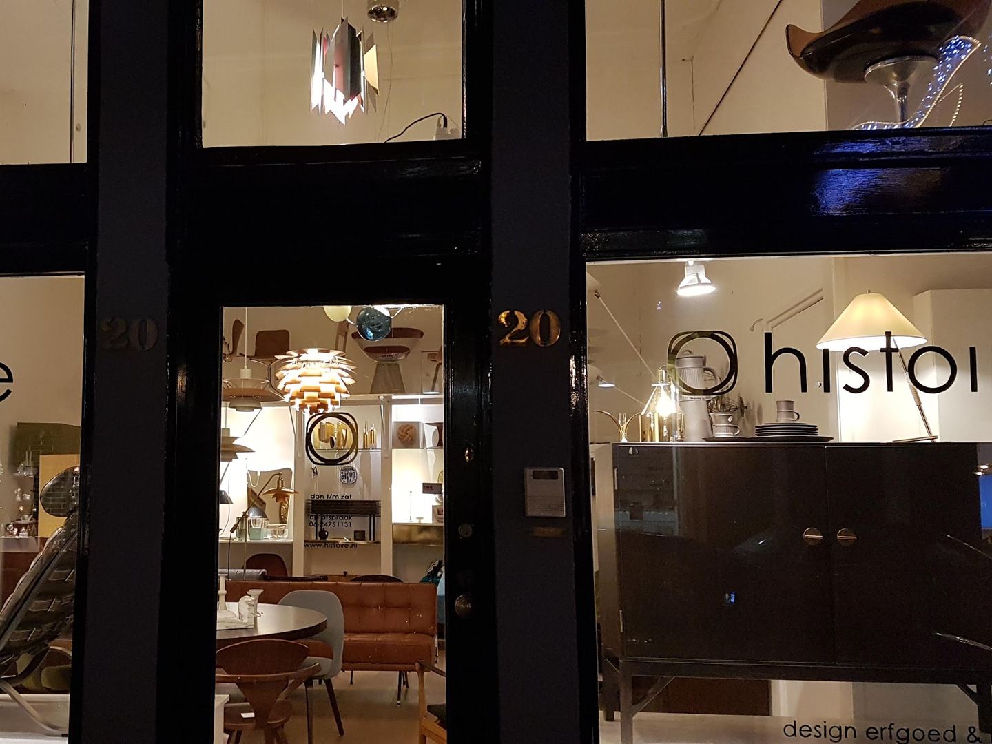 Winkelruimte van Histoire bij avond met vintage designmeubels en lampen achter de ramen