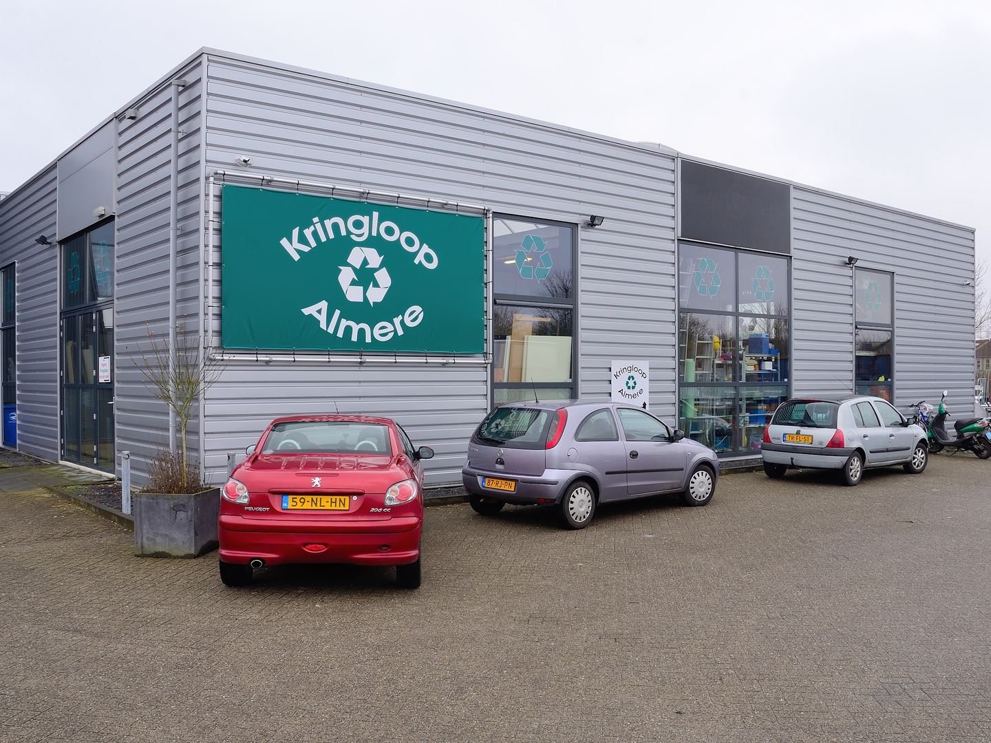 Bedrijfspand van Kringloop Almere met groen naambord boven de ingang en geparkeerde auto's