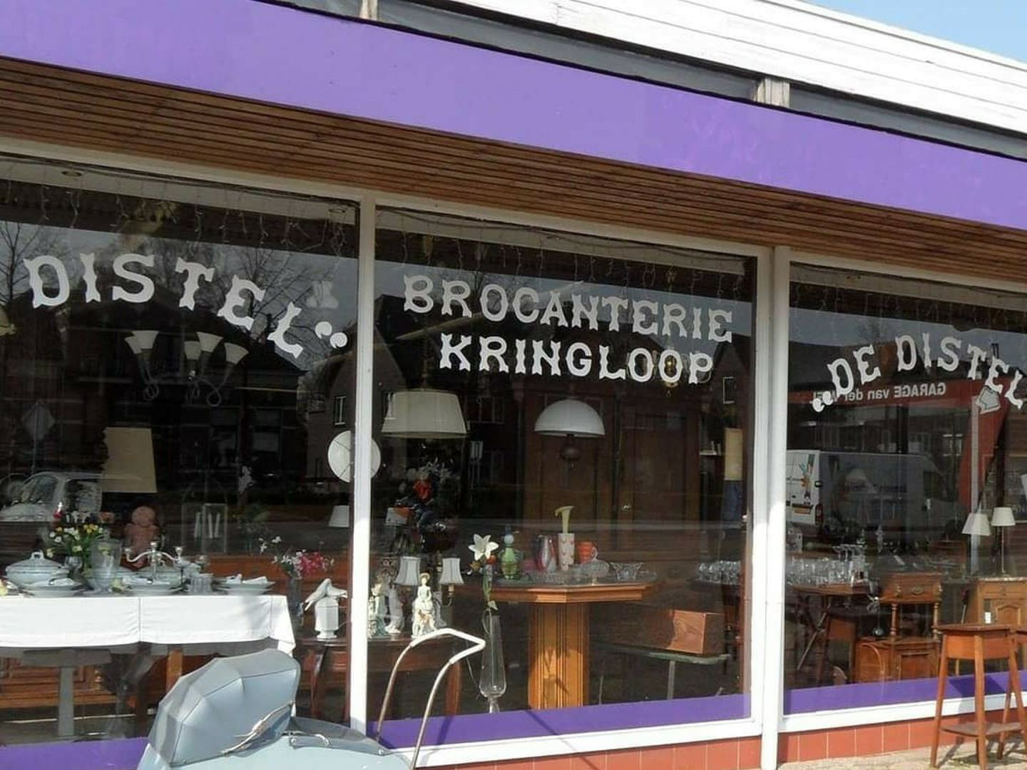 Etalageruiten van De Distel met beschilderde naam en een oude kinderwagen ervoor