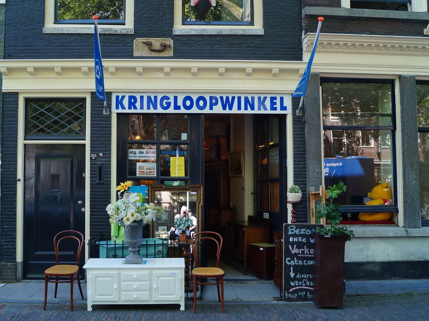 Gevel van de kringloopwinkel aan de Oudegracht met een wit kastje en stoelen voor de deur