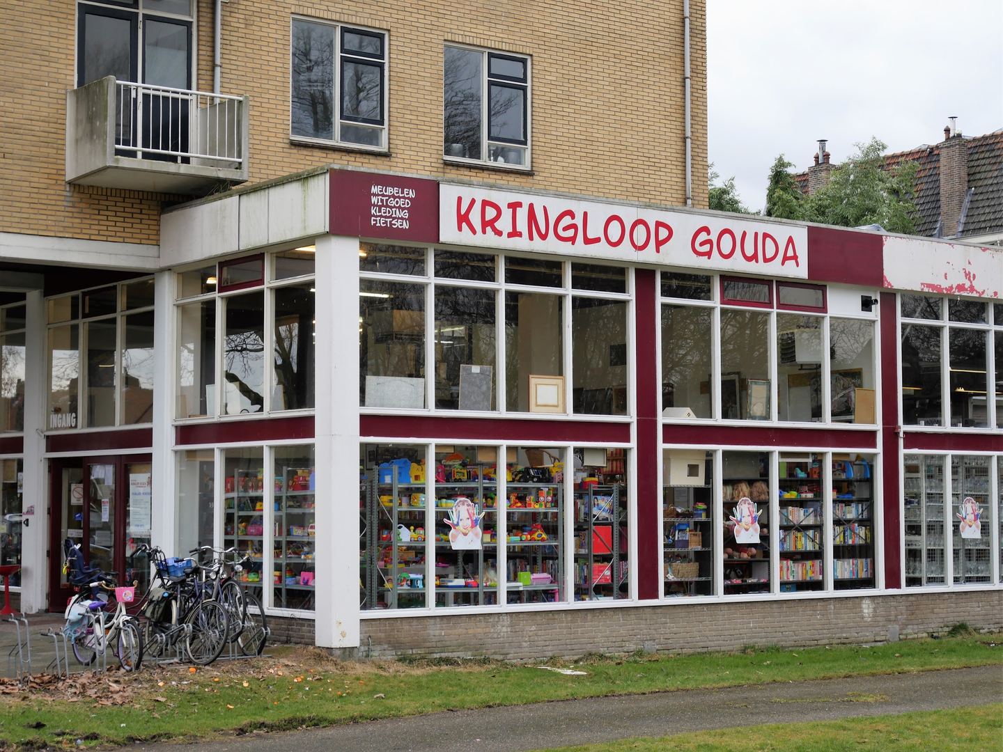 Hoekpand van Kringloop Gouda met rood naambord en grote ramen vol kringloopspullen, fietsen ervoor