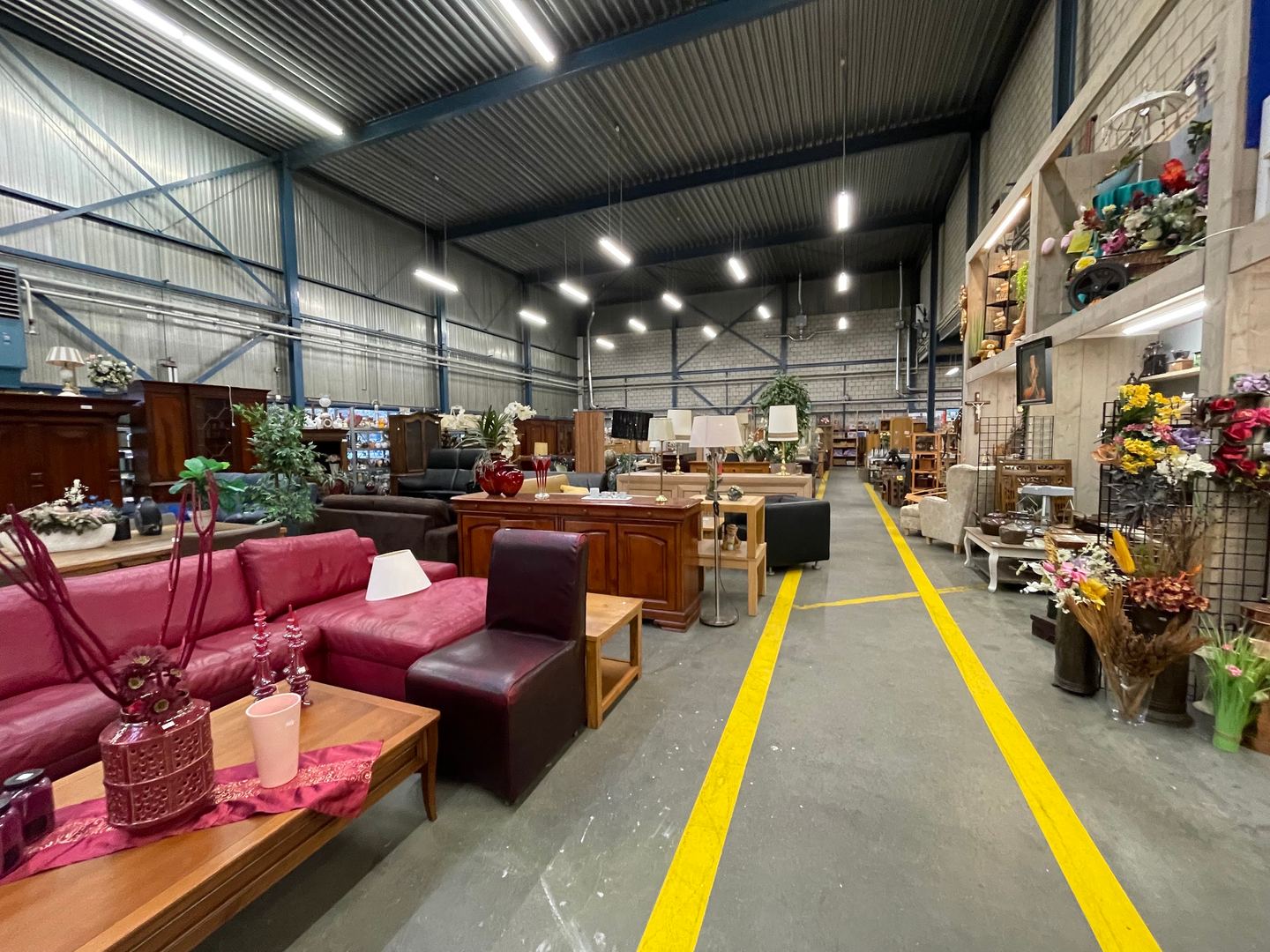 Interieur van de grote kringloophal met banken, kasten en tafels langs een looppad met gele lijnen