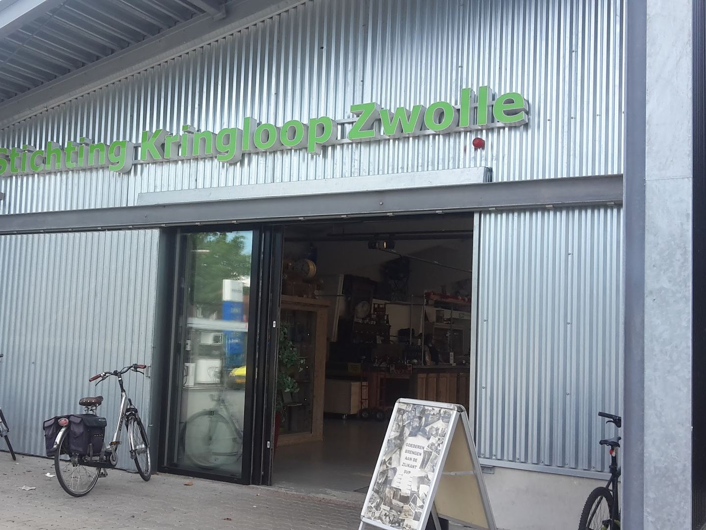Gevel van golfplaat met groene letters Stichting Kringloop Zwolle, een open deur en fietsen ervoor