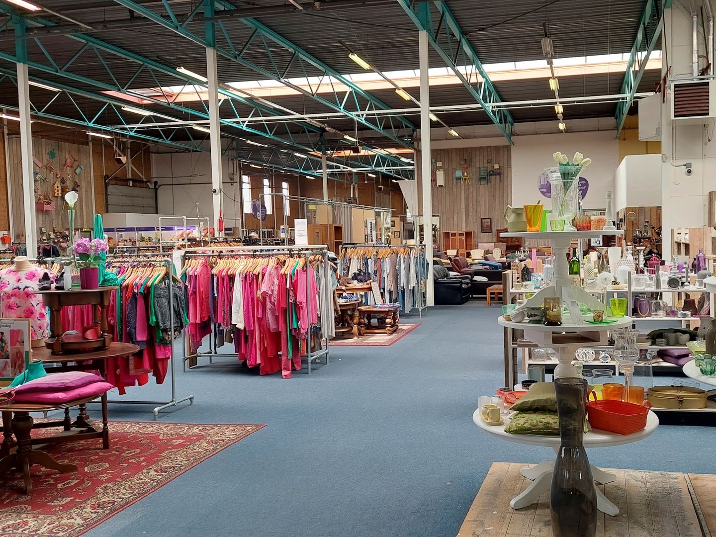 Interieur van Kringloopwarenhuis Het Goed met kledingrekken, glaswerk en woonaccessoires in een grote hal