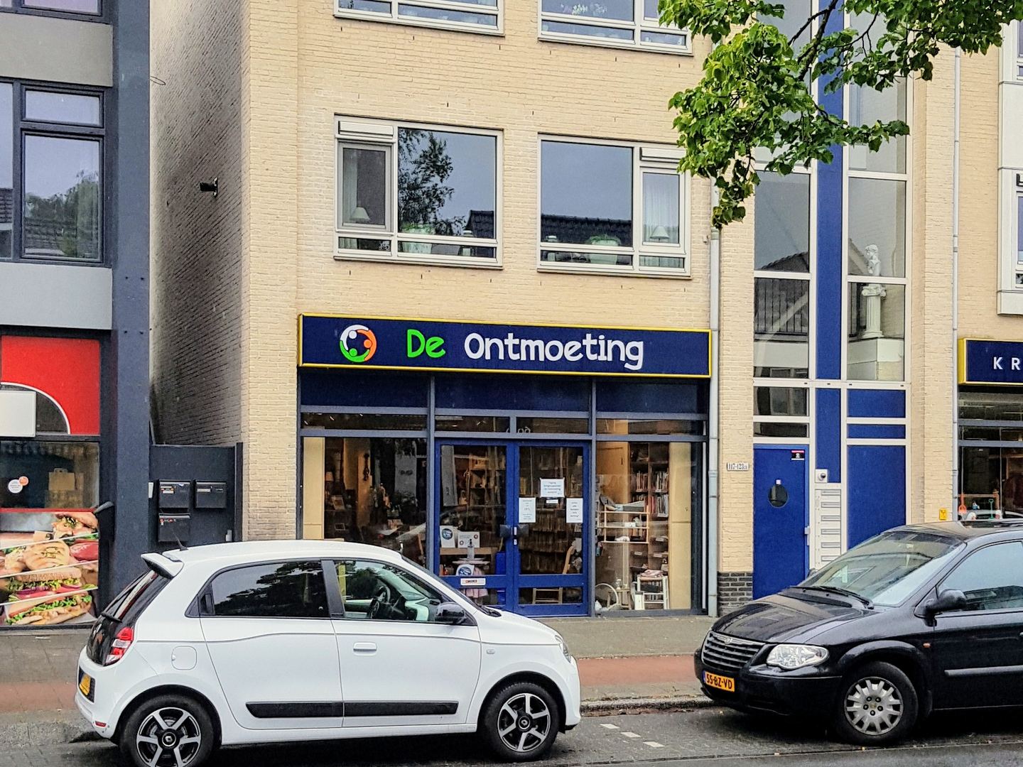Kringloopwinkel De Ontmoeting op de begane grond van een appartementengebouw, met blauw naambord boven de etalage