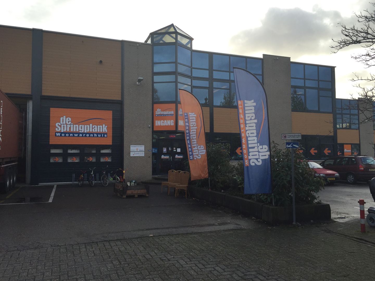 Gevel van Kringloopwinkel de Springplank met oranje naambord en vlaggen bij de ingang