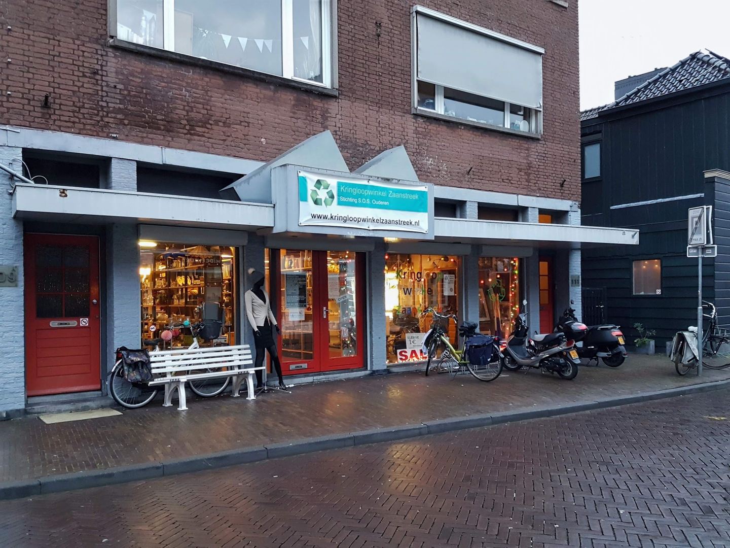 Winkelpui van Kringloopwinkel Zaanstreek met naambord, etalages en een bankje voor de deur