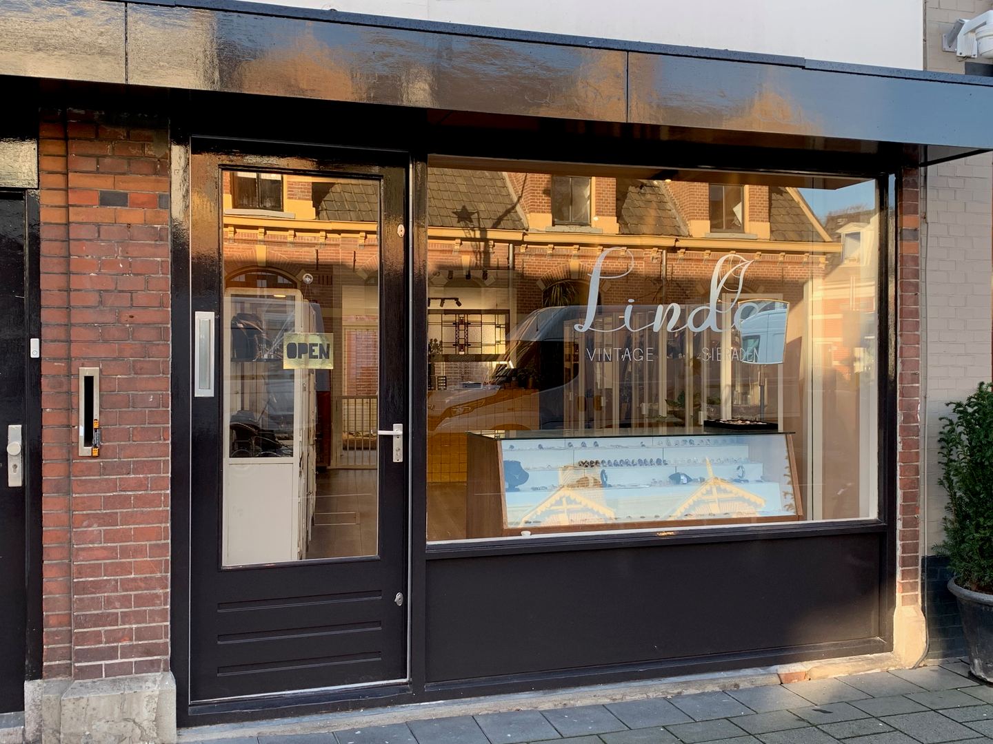 Zwarte winkelpui van Linde met de naam op de etalageruit, een vitrine met sieraden en een open-bordje op de deur