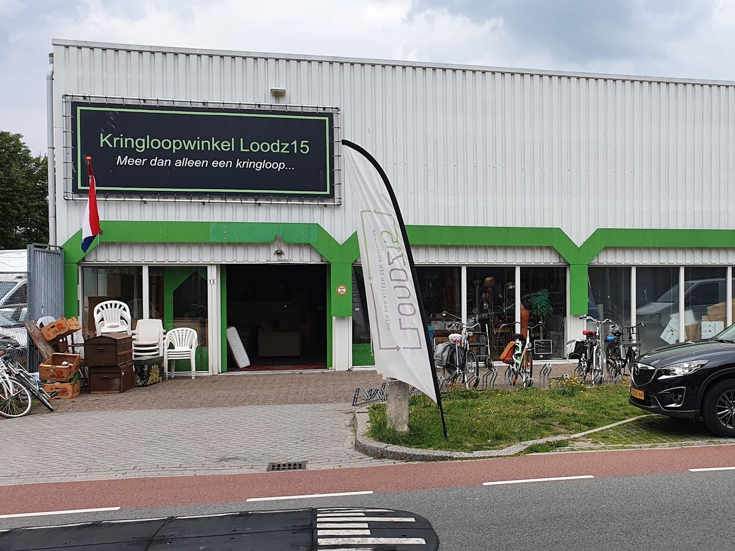 Gevel van Kringloopwinkel Loodz15 met groen-wit bedrijfspand, naambord en vlag bij de ingang