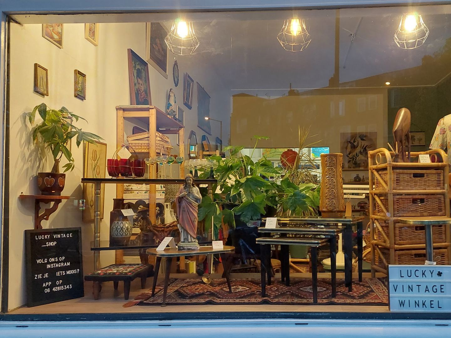 Etalage van Lucky Vintage met rotan meubels, planten, kleding en een bordje met de winkelnaam