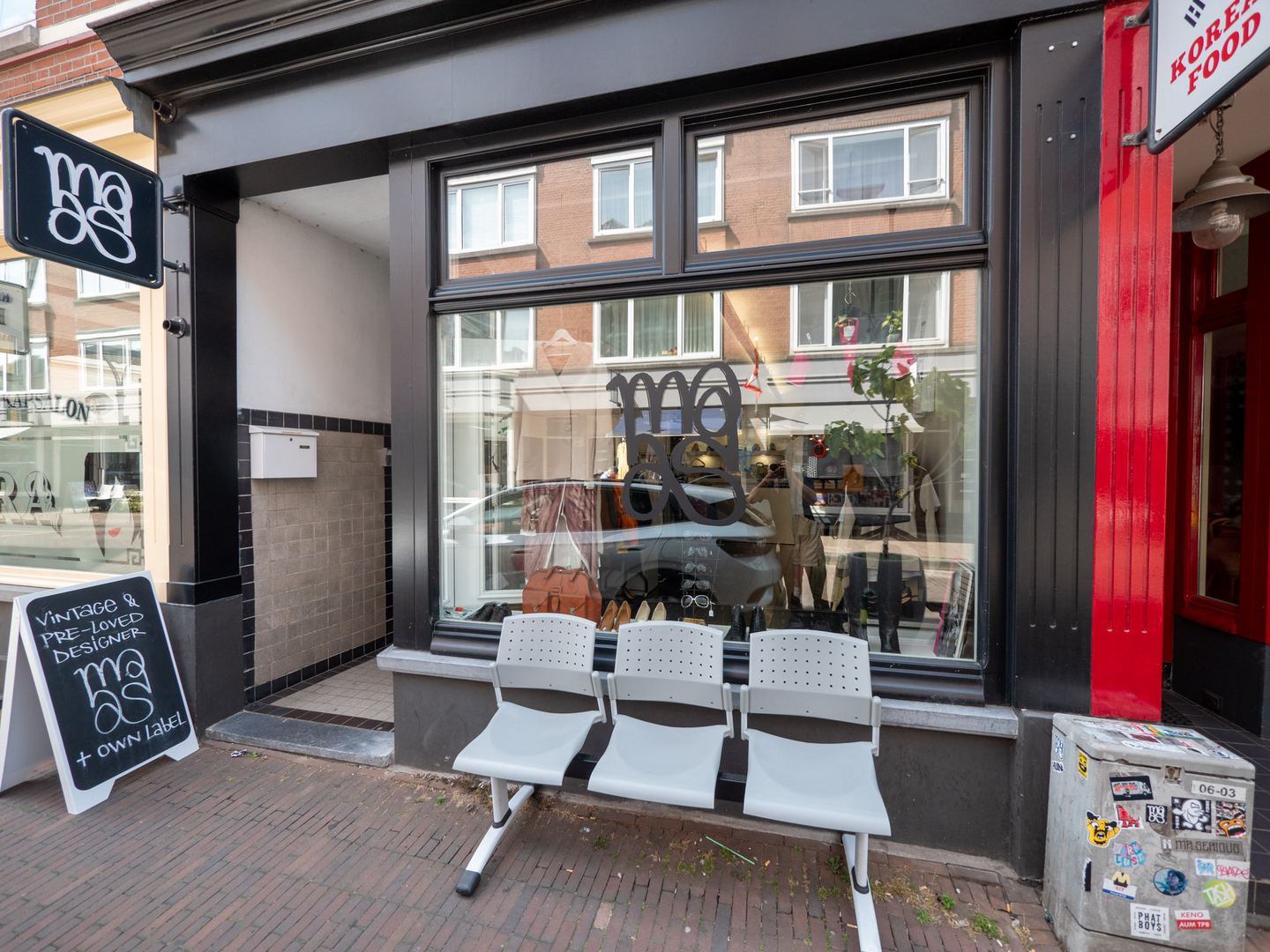 Gevel van Maison Maas met logo in het raam, een stoepbord en stoelen voor de etalage