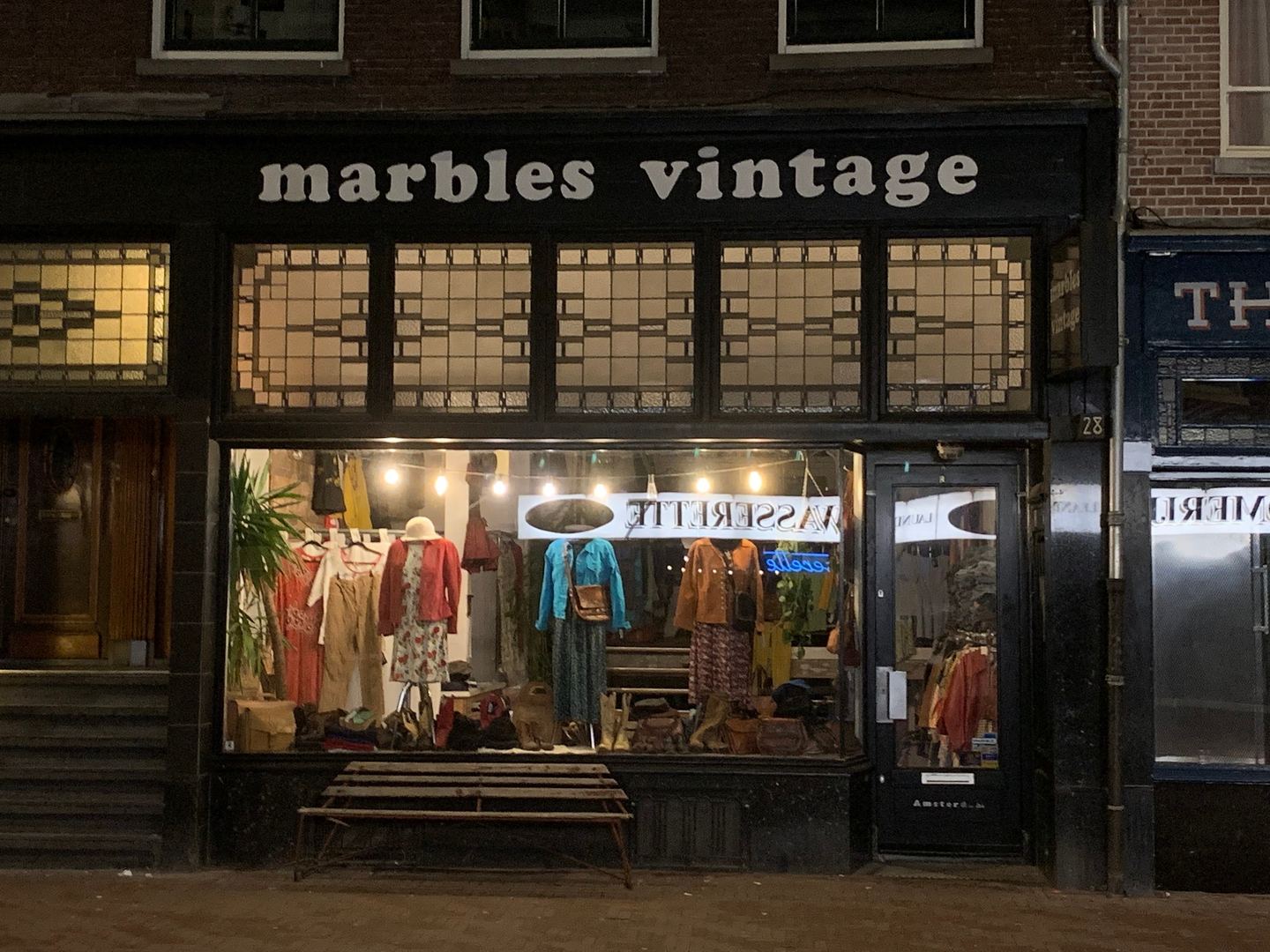 Gevel van Marbles Vintage met verlichte etalage vol vintage kleding en tassen