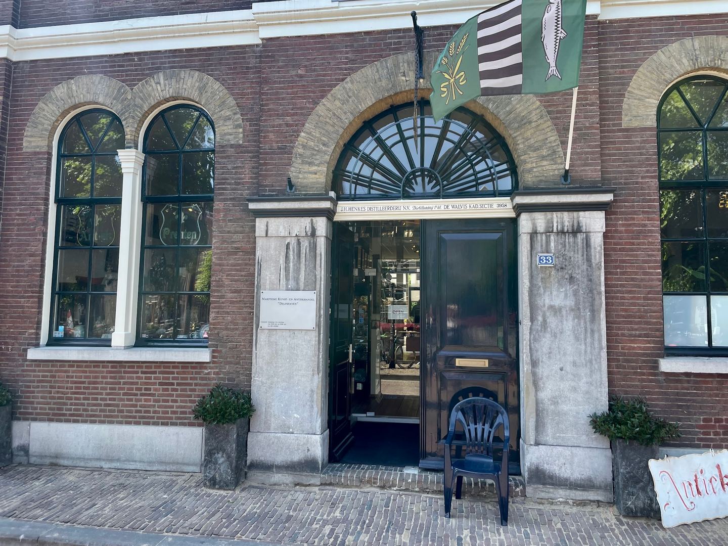 Historische bakstenen gevel van de maritieme antiekhandel met open voordeur en vlaggen boven de ingang