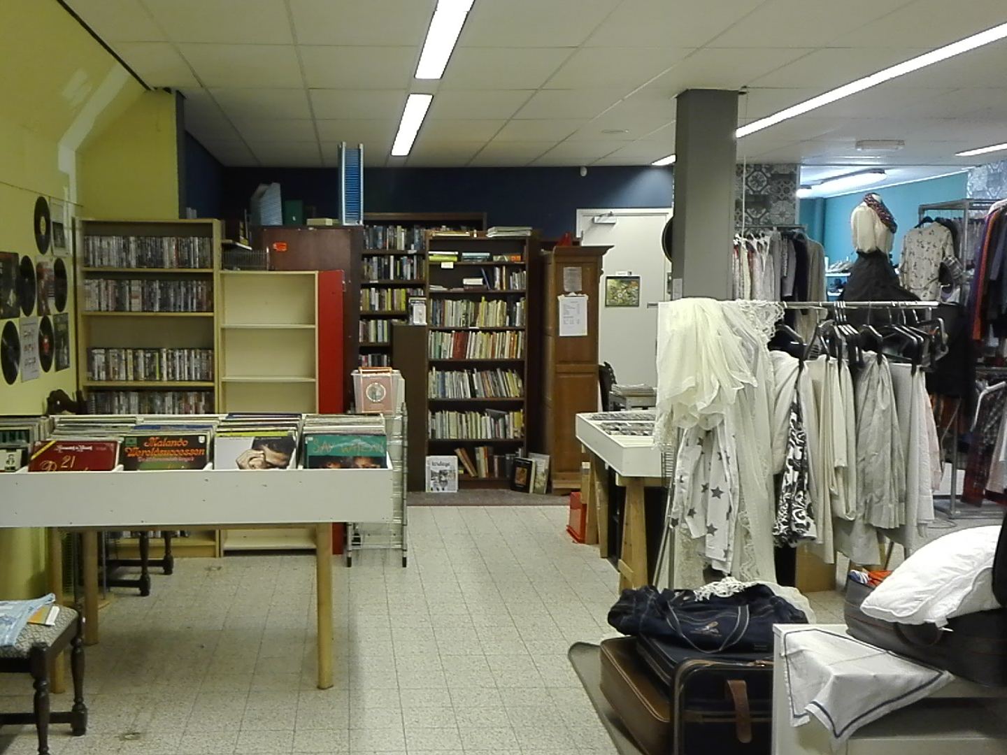Interieur van de kringloopwinkel met bakken lp's, boekenkasten en rekken met kleding