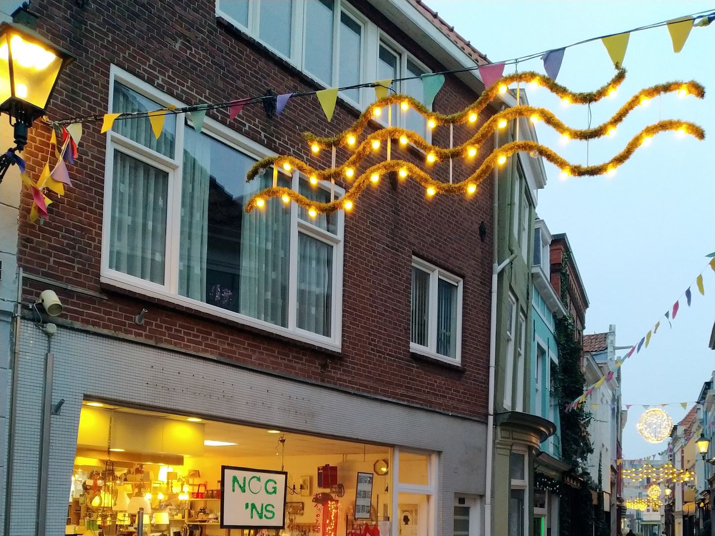 Gevel van Nog 'ns met verlichte etalage vol tweedehands spullen