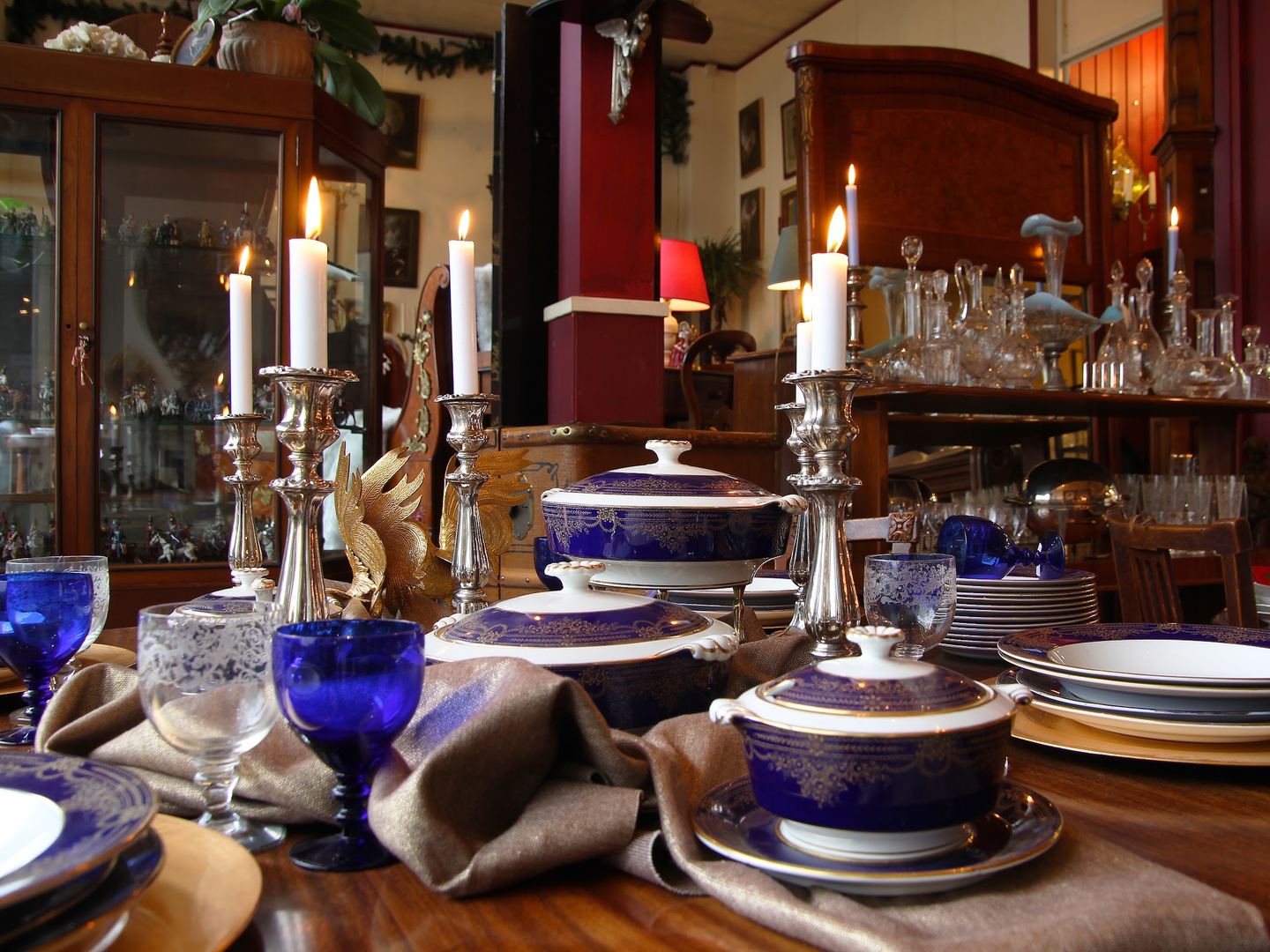 Showroom van Notre Dame Antiek met een gedekte tafel vol servies, kristal en kandelaars voor antieke kasten