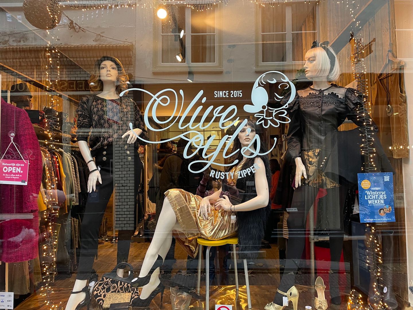 Etalage van Olive Oyl's Rusty Zipper met het logo op de ruit en paspoppen in jurken en jassen