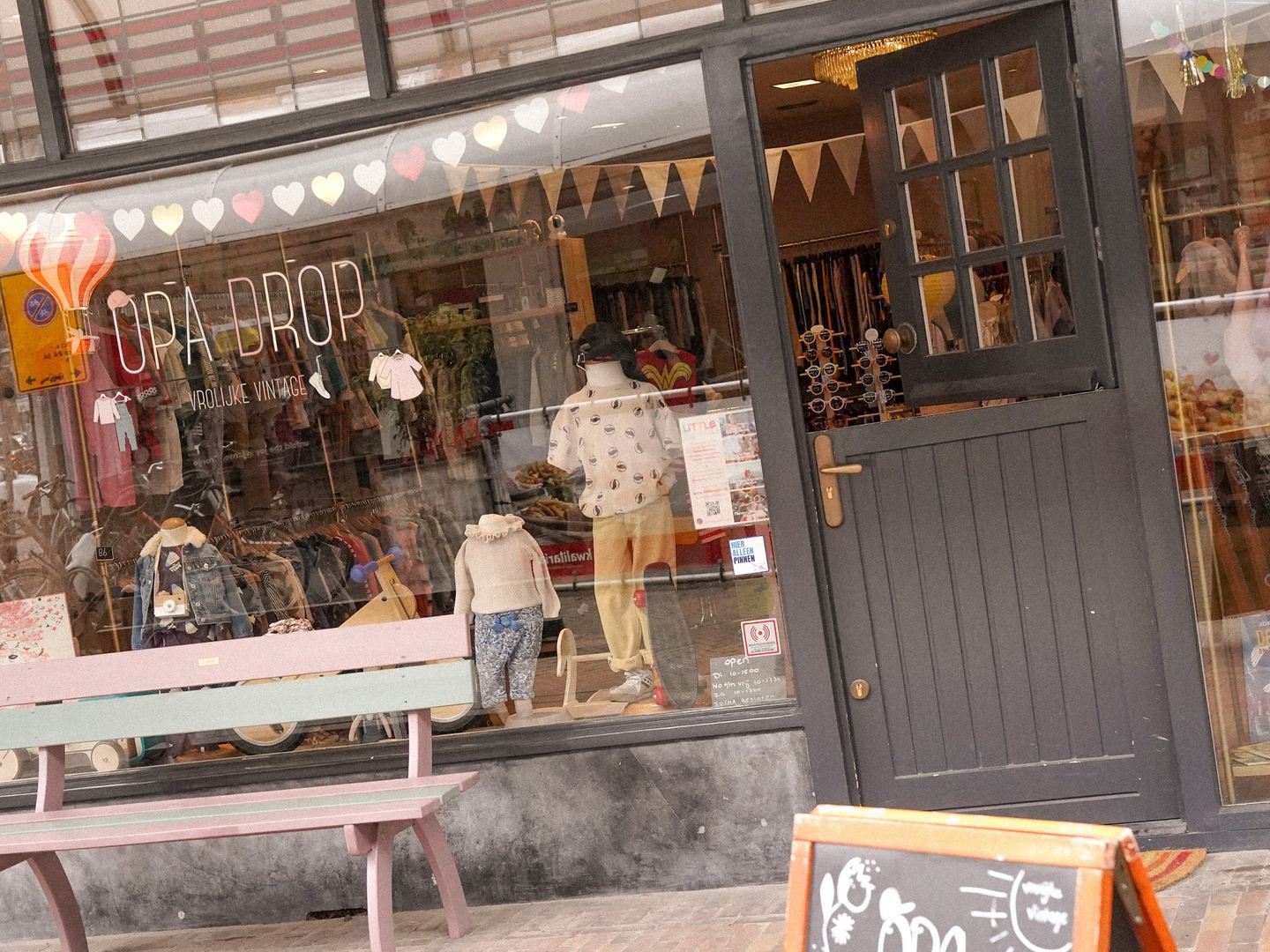 Gevel van Opa Drop met kinderkleding in de etalage, een bankje en een krijtbord voor de deur
