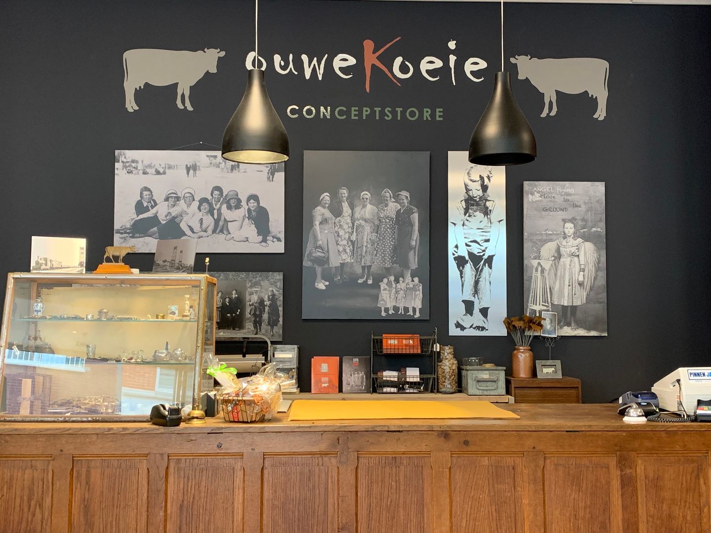 Toonbank van Ouwe Koeie Conceptstore met het logo aan de muur, een vitrinekast en oude familiefoto's