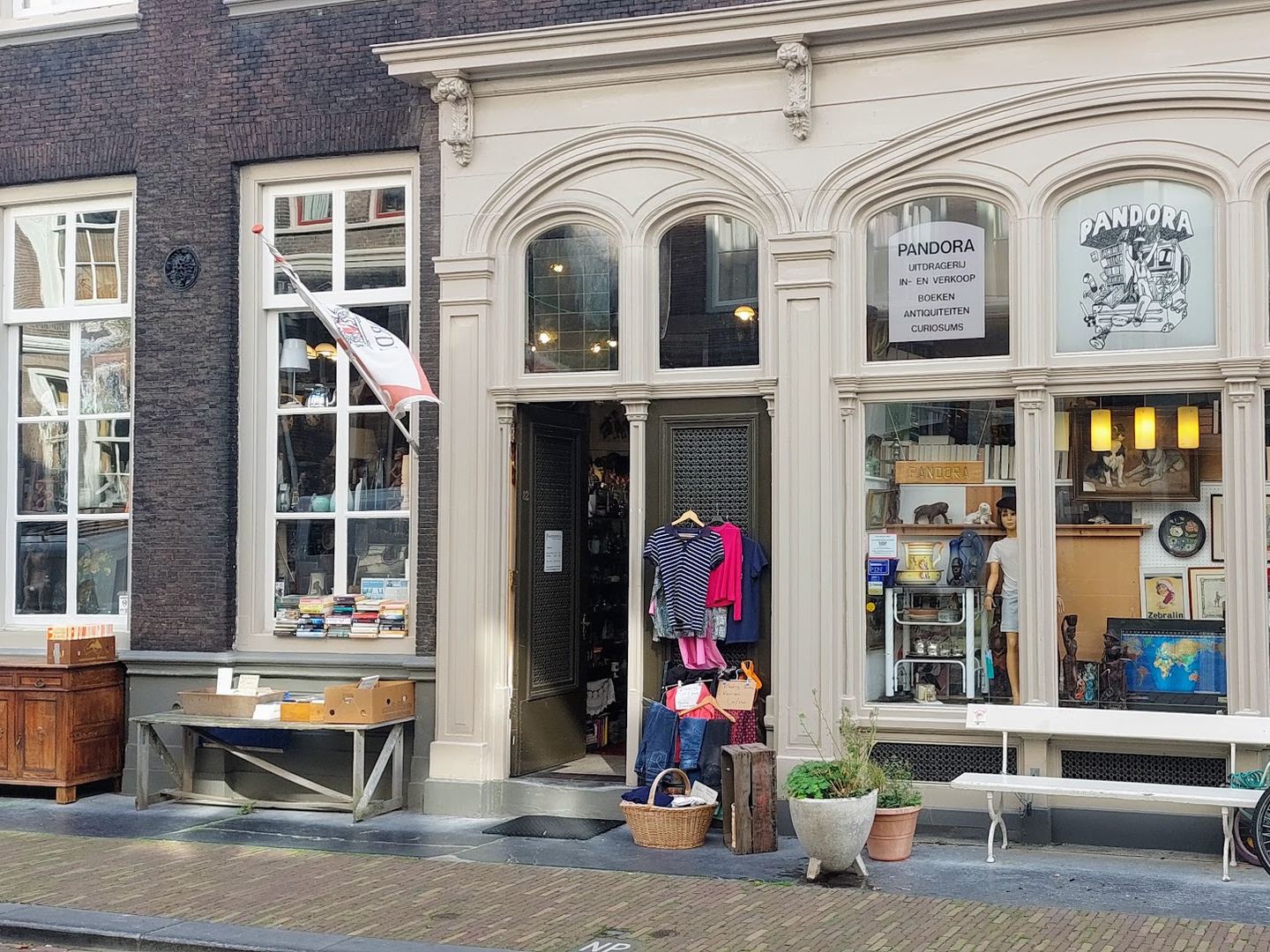 Witte winkelpui van Pandora met etalages vol curiosa, kleding aan de deur en een bankje voor de gevel