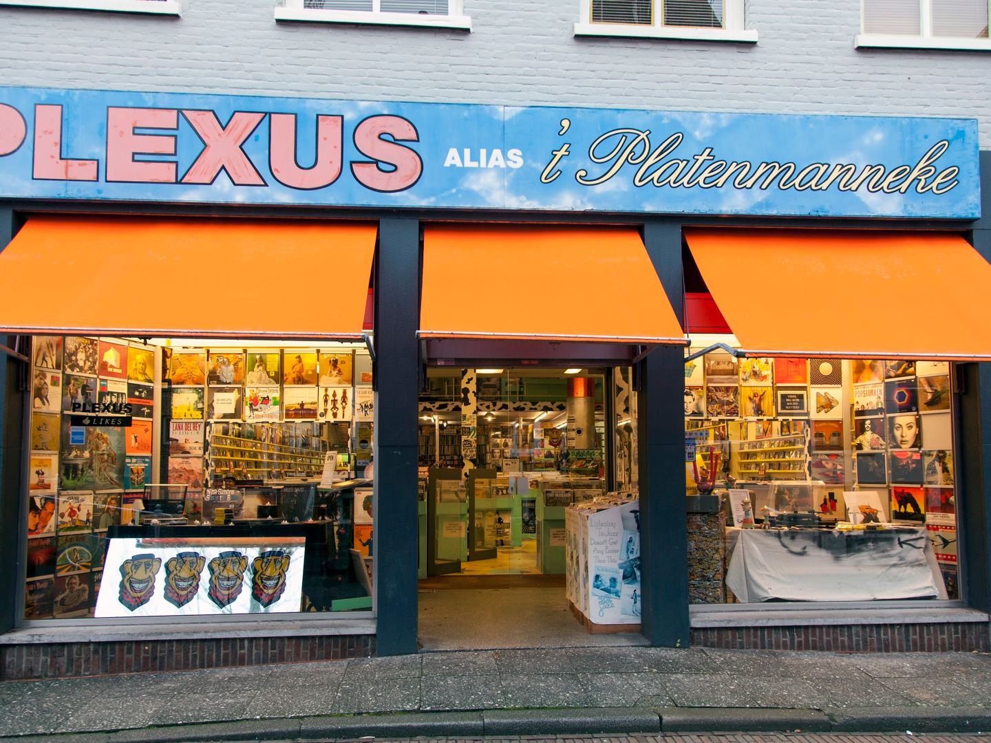 Winkelpui van Plexus met oranje luifels, naambord en etalages vol platenhoezen