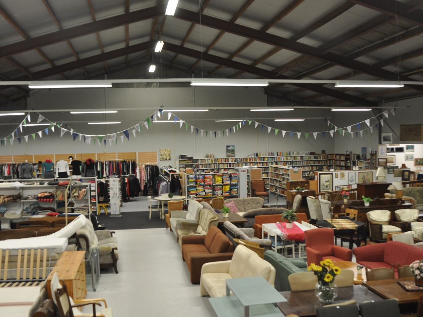 Grote kringloophal van Ramsjburg met banken, fauteuils, kledingrekken en boekenkasten onder vlaggetjes