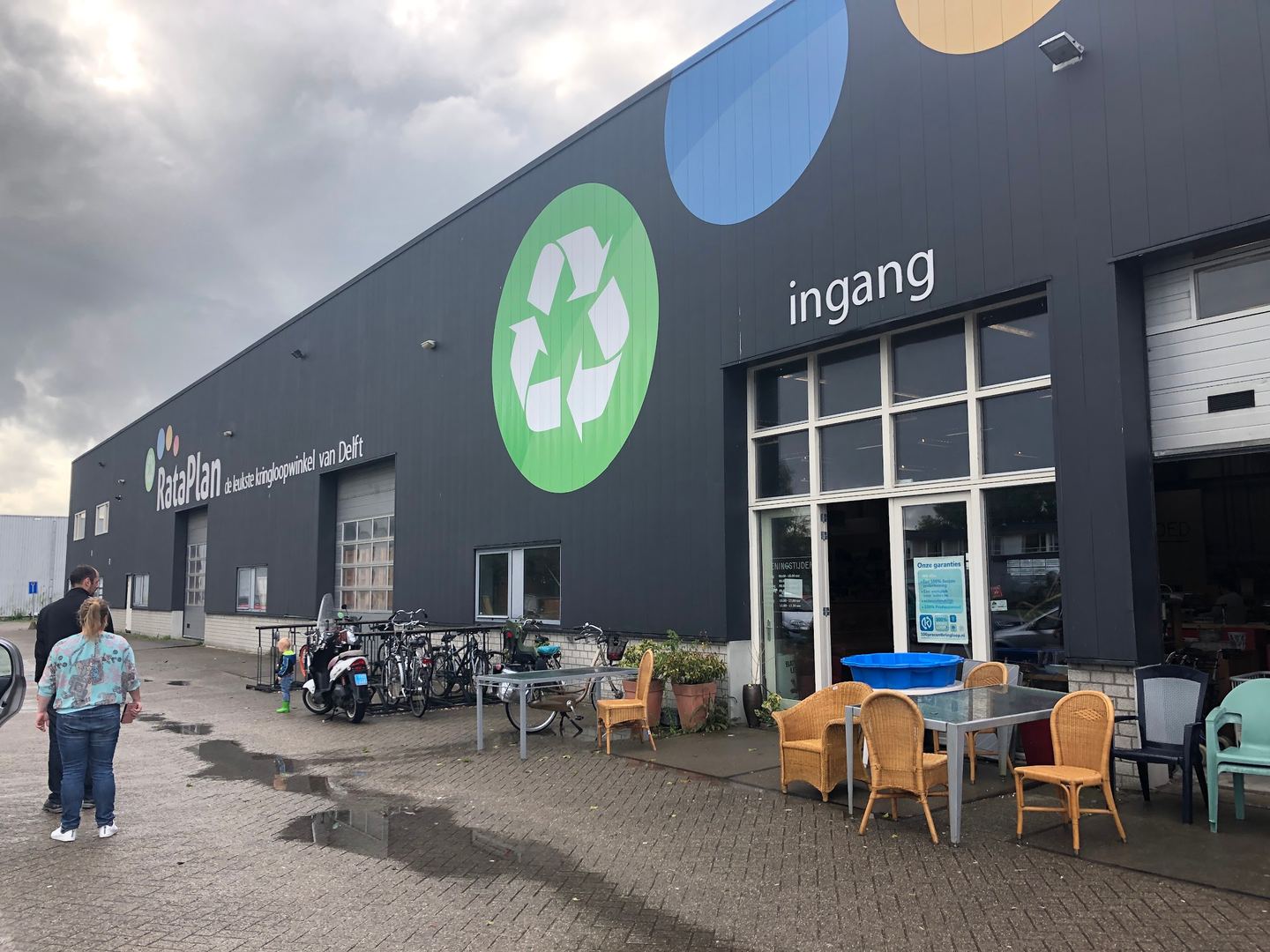 Donkere gevel van RataPlan met kringloopsymbool, ingang en tuinmeubels voor de deur