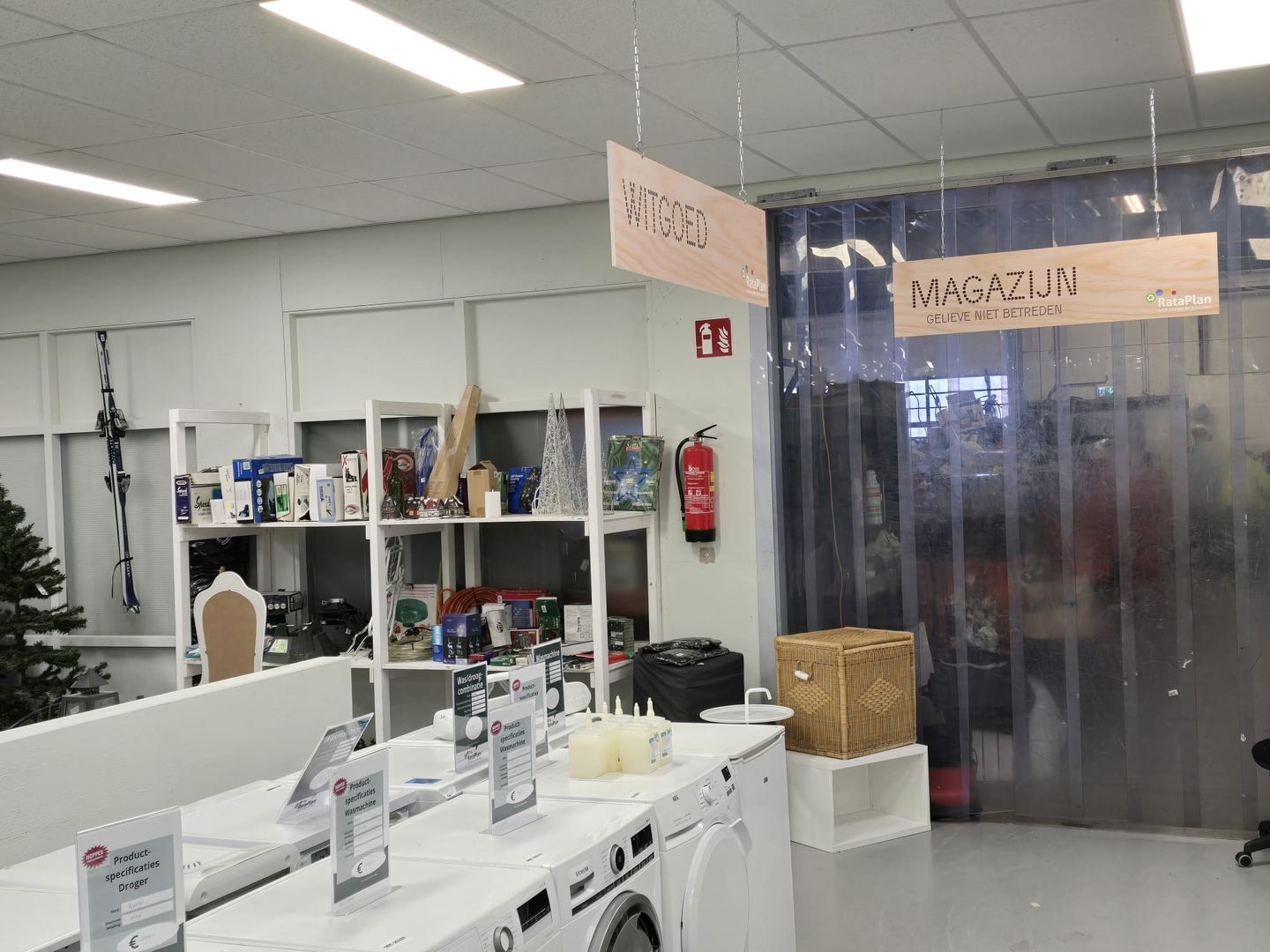 Interieur van Kringloopwinkel RataPlan met witgoedafdeling, wasmachines en schappen met huishoudspullen